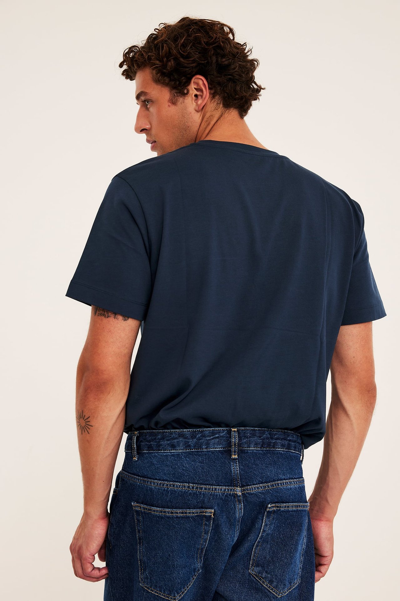 Bakfra av voksen mann i mørkeblå kortermet t-skjorte og mørkeblå jeans.