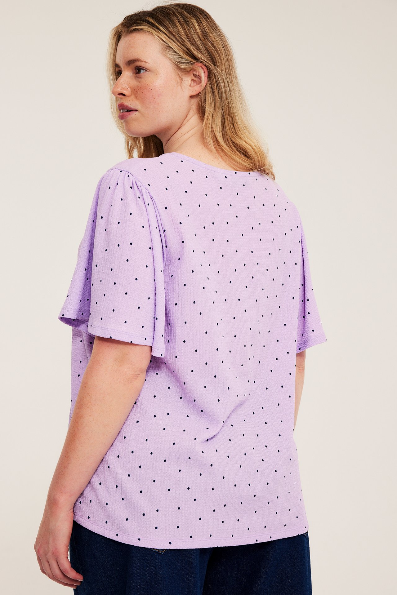 Kvinna i en ljuslila prickig kortärmad topp med puffärmar, sedd bakifrån, och mörka byxor.