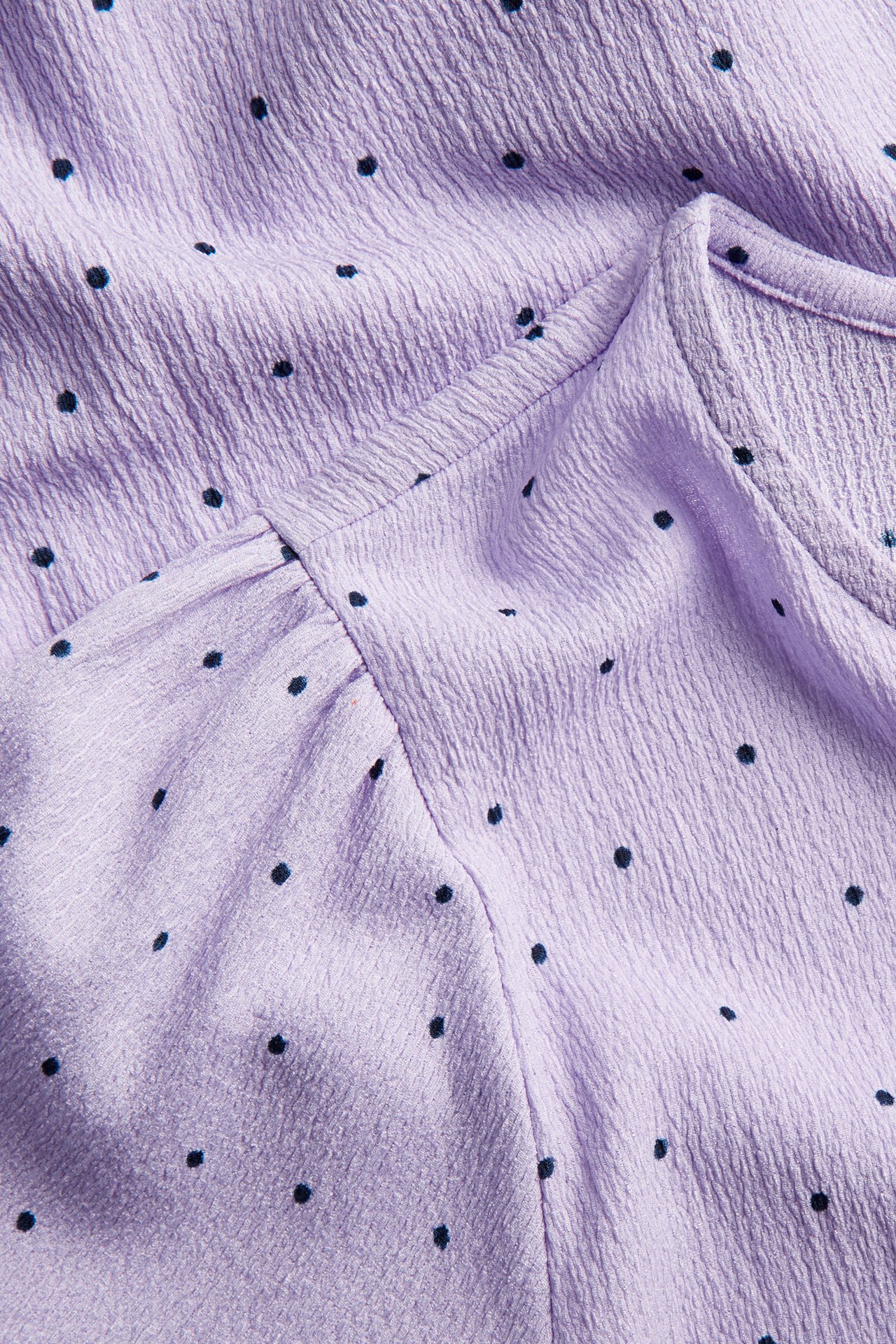 Närbild på en ljuslila kortärmad topp med svarta prickar och krinklad textur.