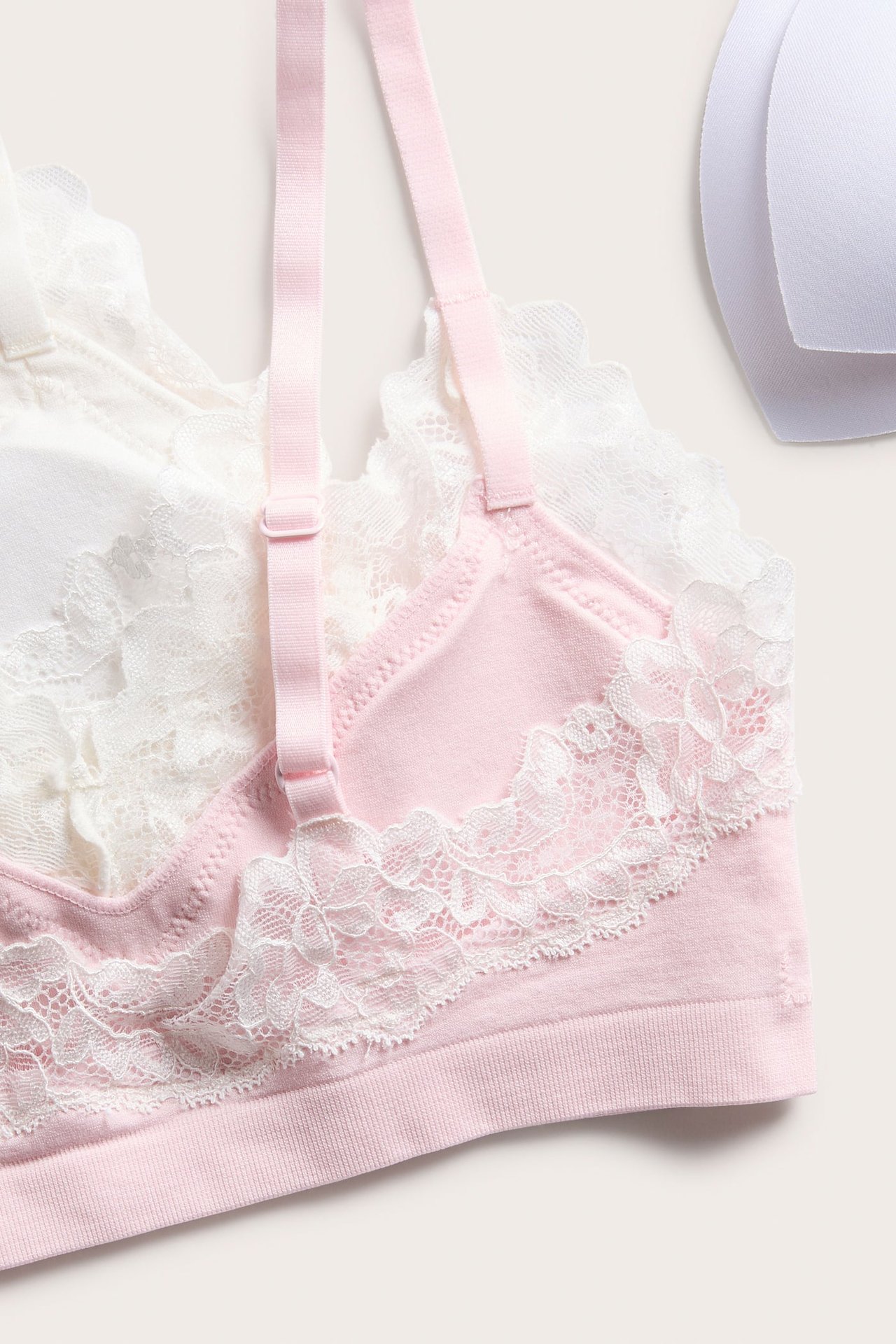 Närbild av en rosa bralette med vit spets, en vit bralette och två vita BH-inlägg.