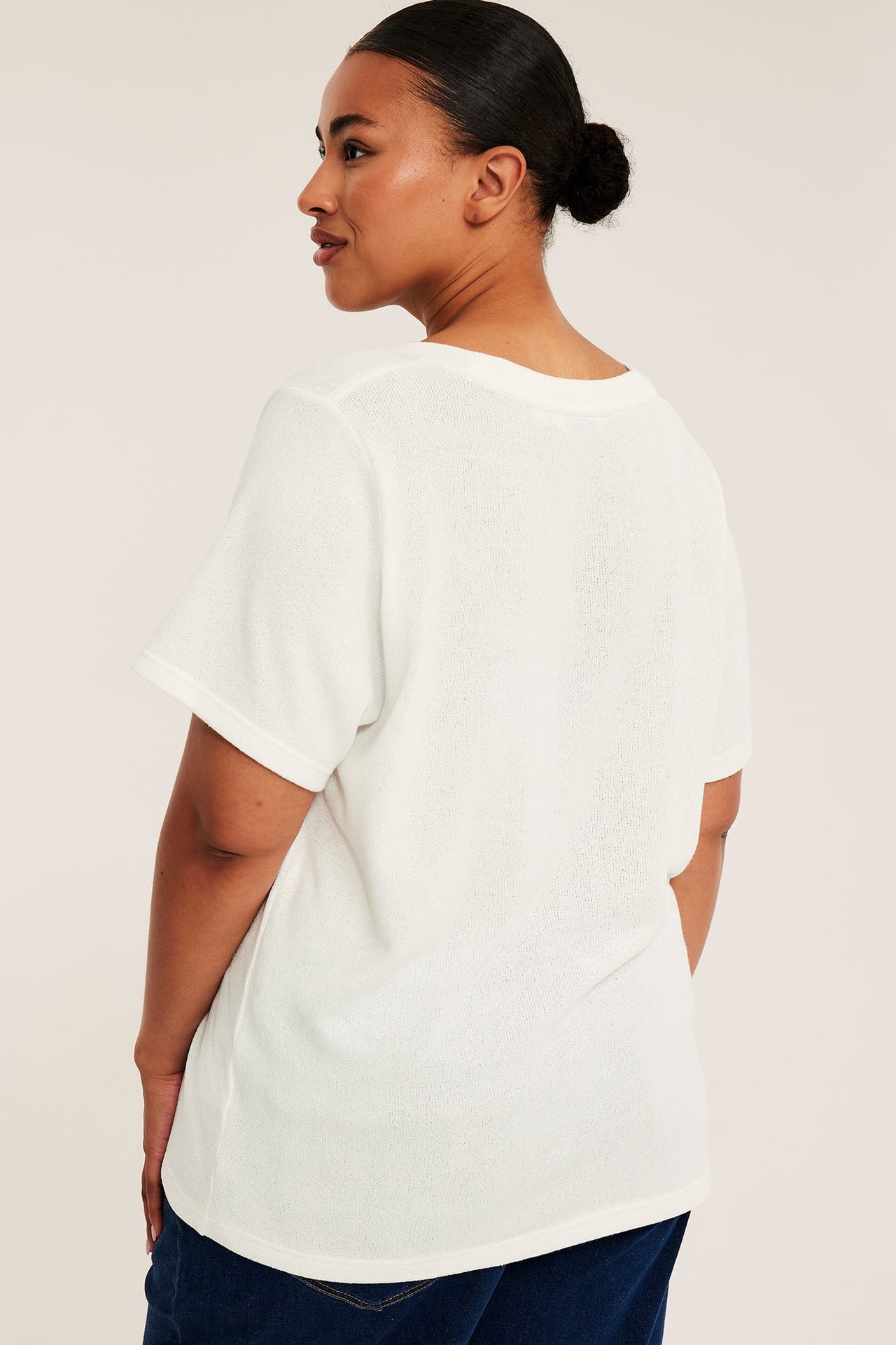 Kvinnelig modell bakfra i en hvit teksturert kortermet topp og mørkeblå jeans.
