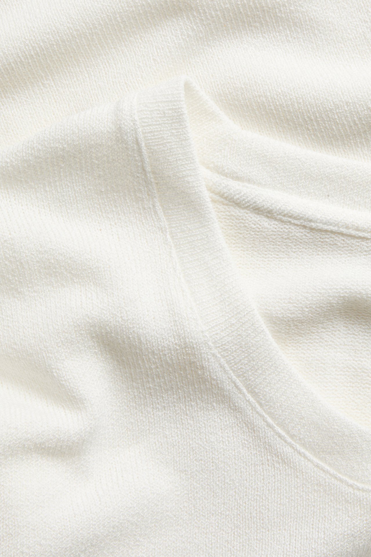 Lähikuva valkoisesta neulemaisesta t-paidasta syvällä pääntieellä, kangasrakenne näkyy.