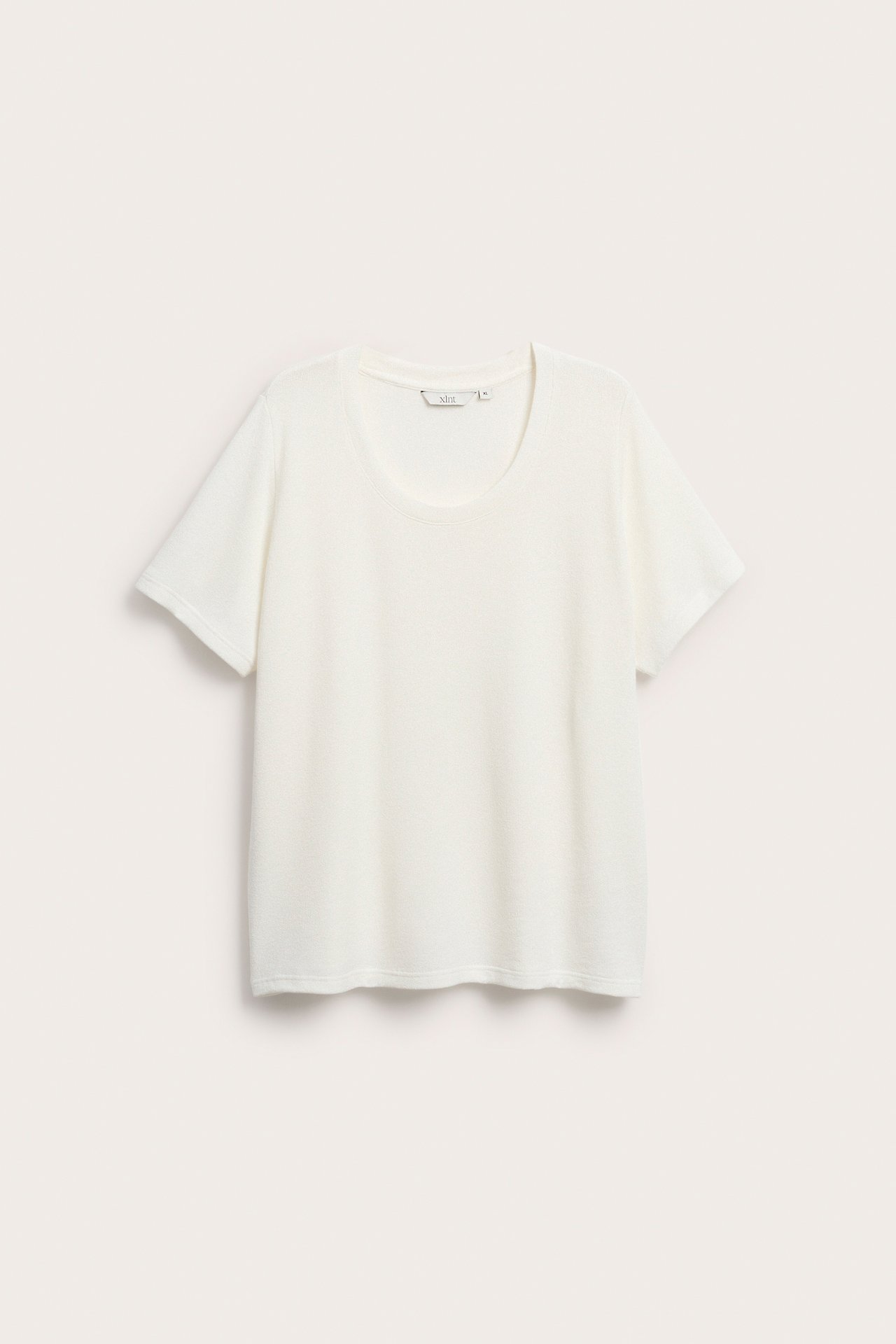 Edestä näkymä valkoisesta, lyhythihaisesta, pyöreäkauluksisesta, rennosti istuvasta neulotusta t-paidasta.