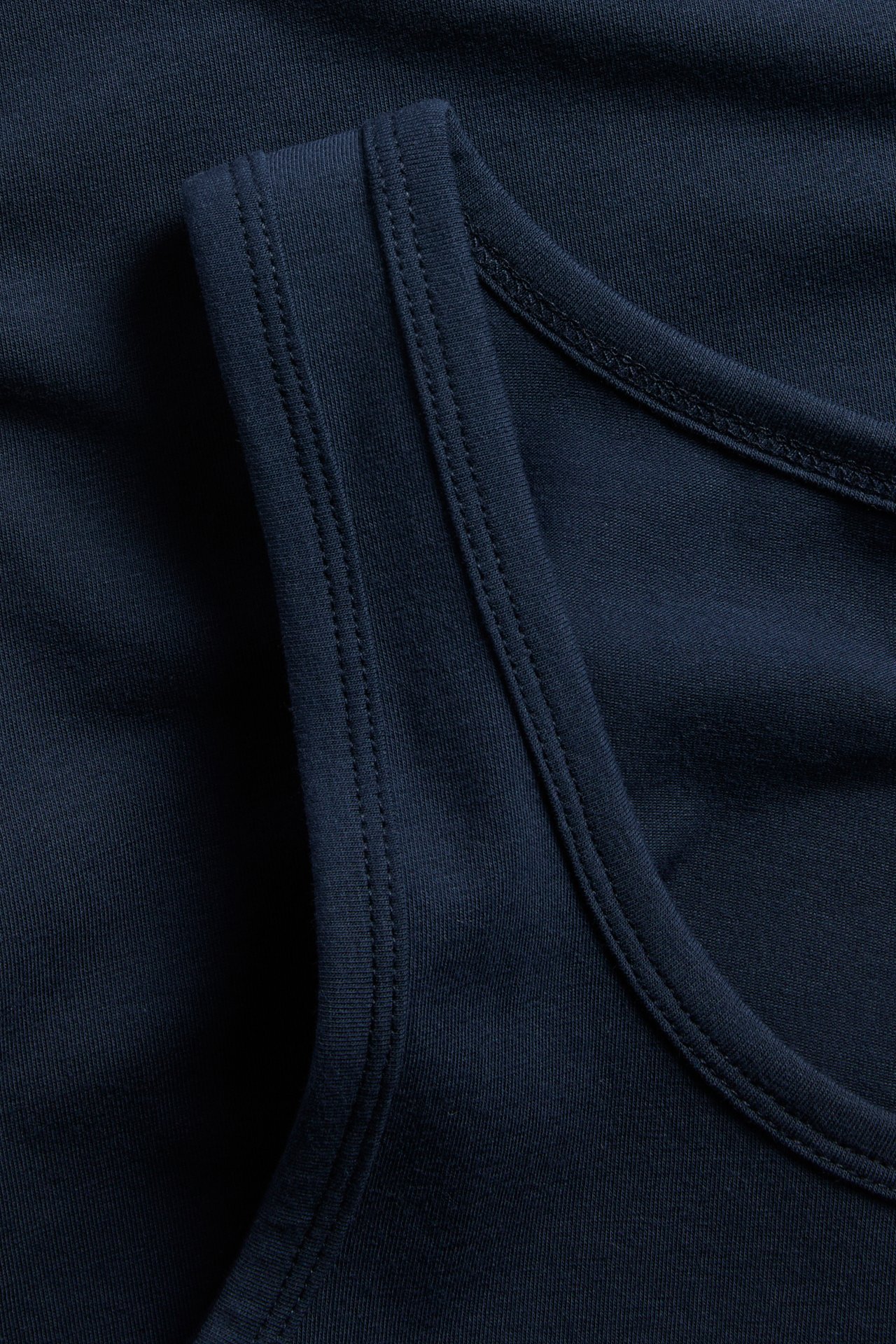 Zbliżenie na granatowy bawełniany top z dzianiny, ukazujące teksturę materiału i szczegółowe przeszycia.