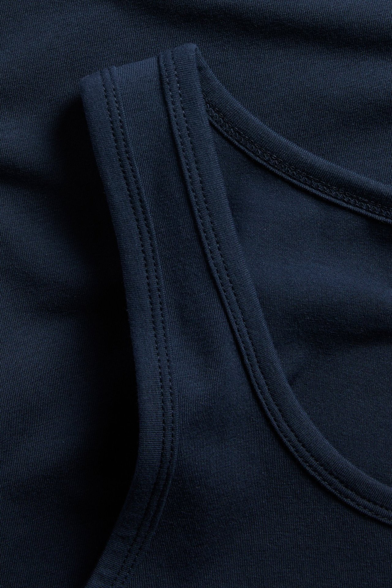 Närbild av ett mörkblått linne i bomullstrikå, som visar tygets struktur och detaljerade sömmar.