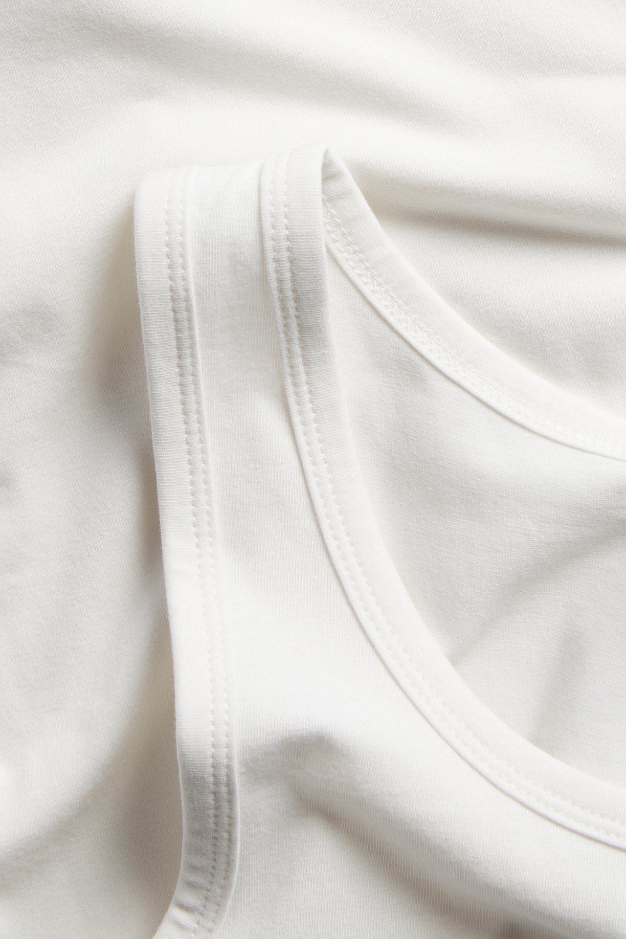 Lähikuva valkoisesta puuvillaneuletopista, näyttäen pääntien ja olkahihnan.