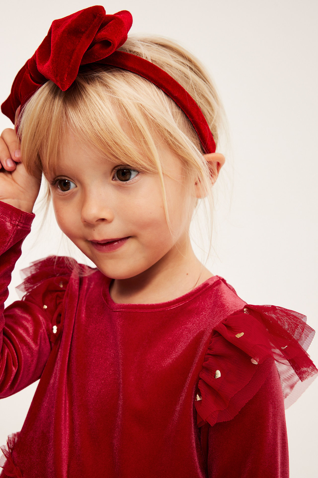 Dziecko w czerwonej aksamitnej sukience z tiulowymi falbankami, złotymi serduszkami i czerwonej opasce z kokardą.
