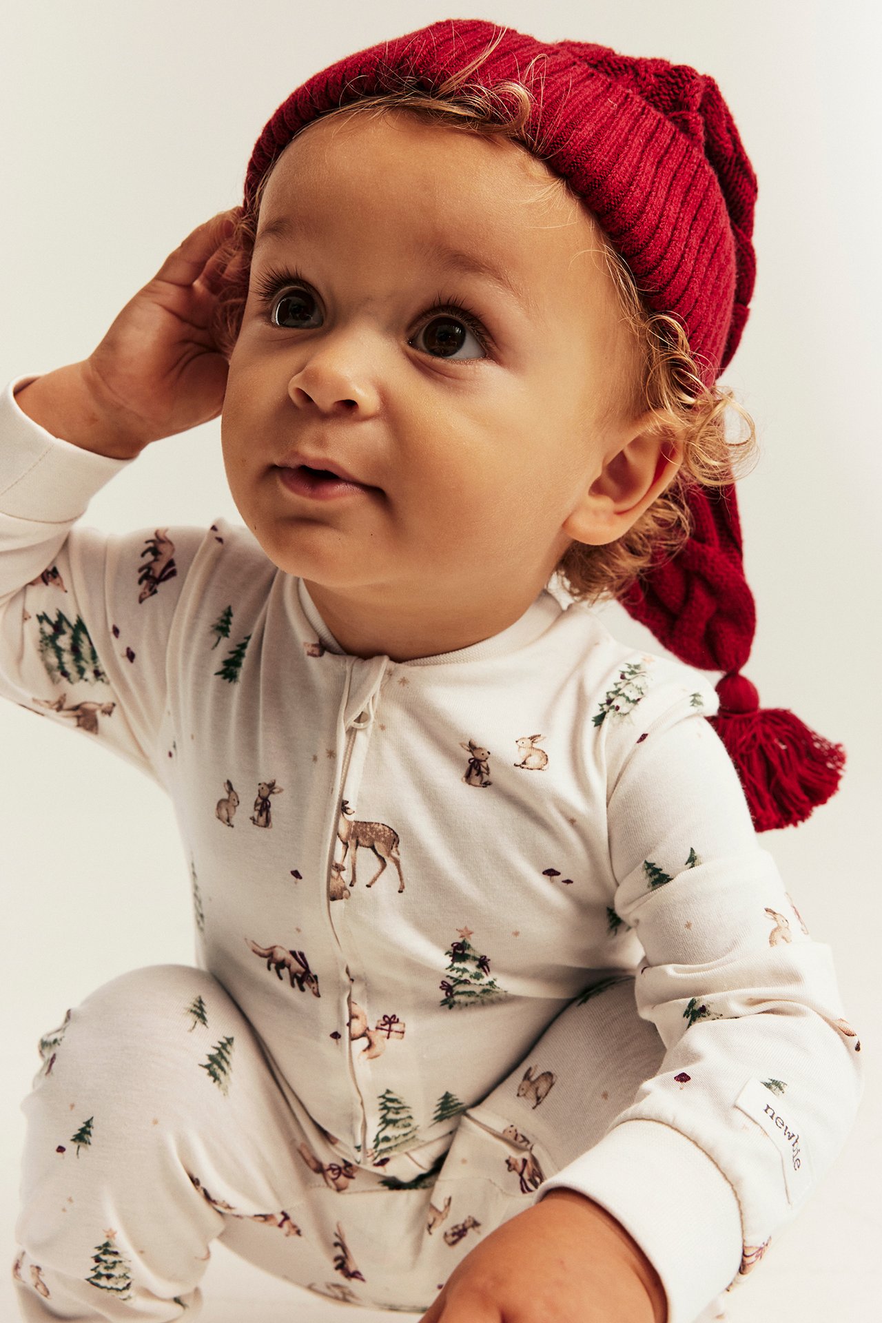 Närbild på baby i vit pyjamas med skogstryck och röd ribbad mössa.