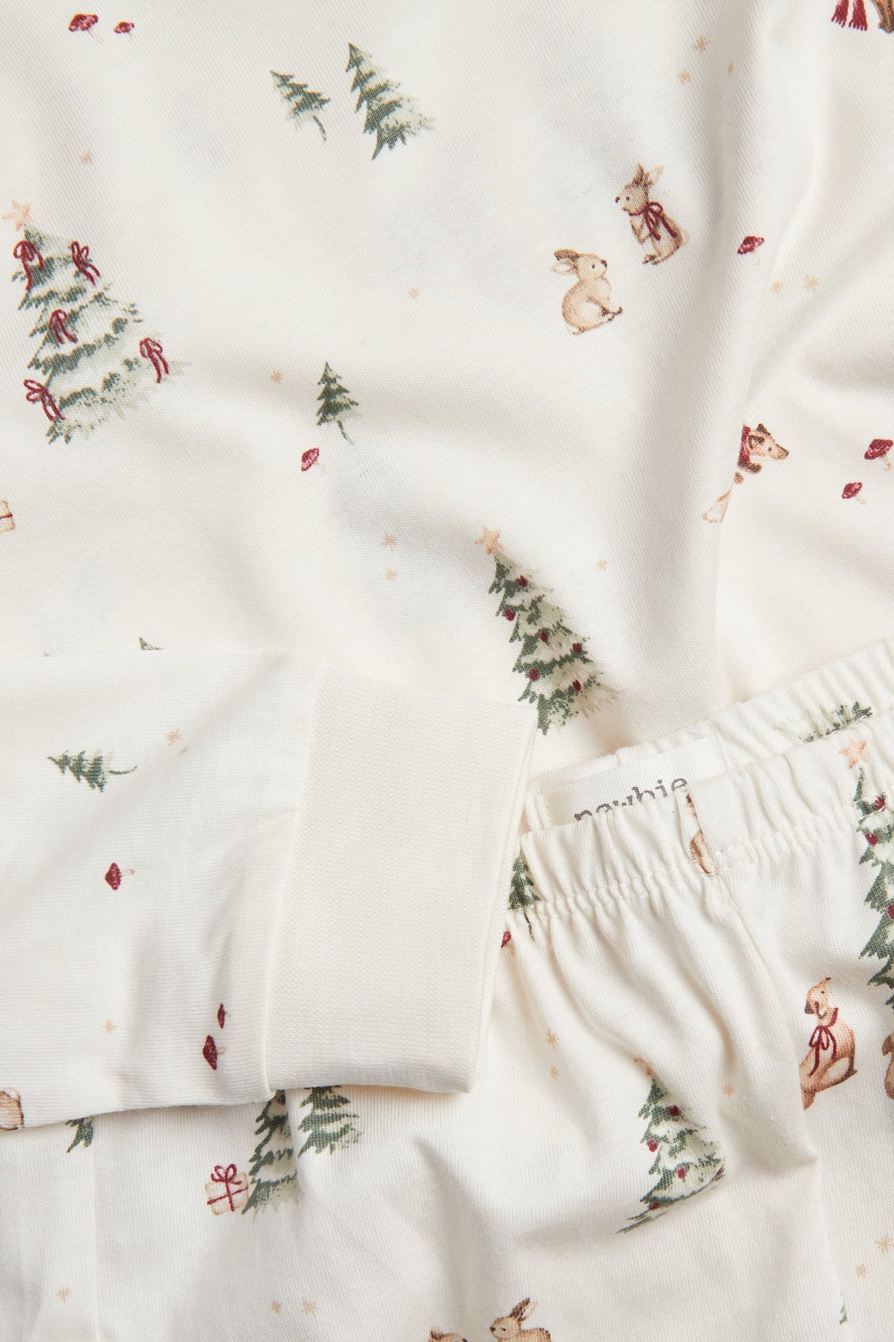 Närbild på vit pyjamas för baby med julskogsprint, med träd och kaniner.