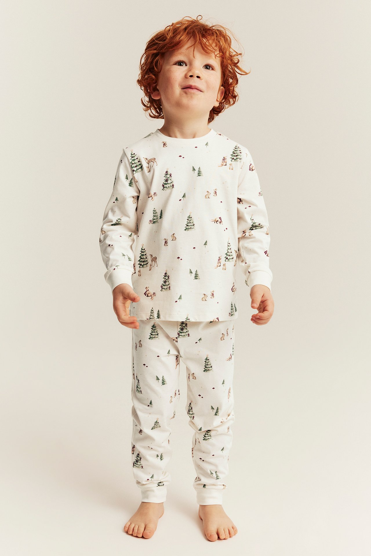 Edestä näkymä lapsesta valkoisessa pyjamassa, jossa on metsäeläin- ja puukuosi.