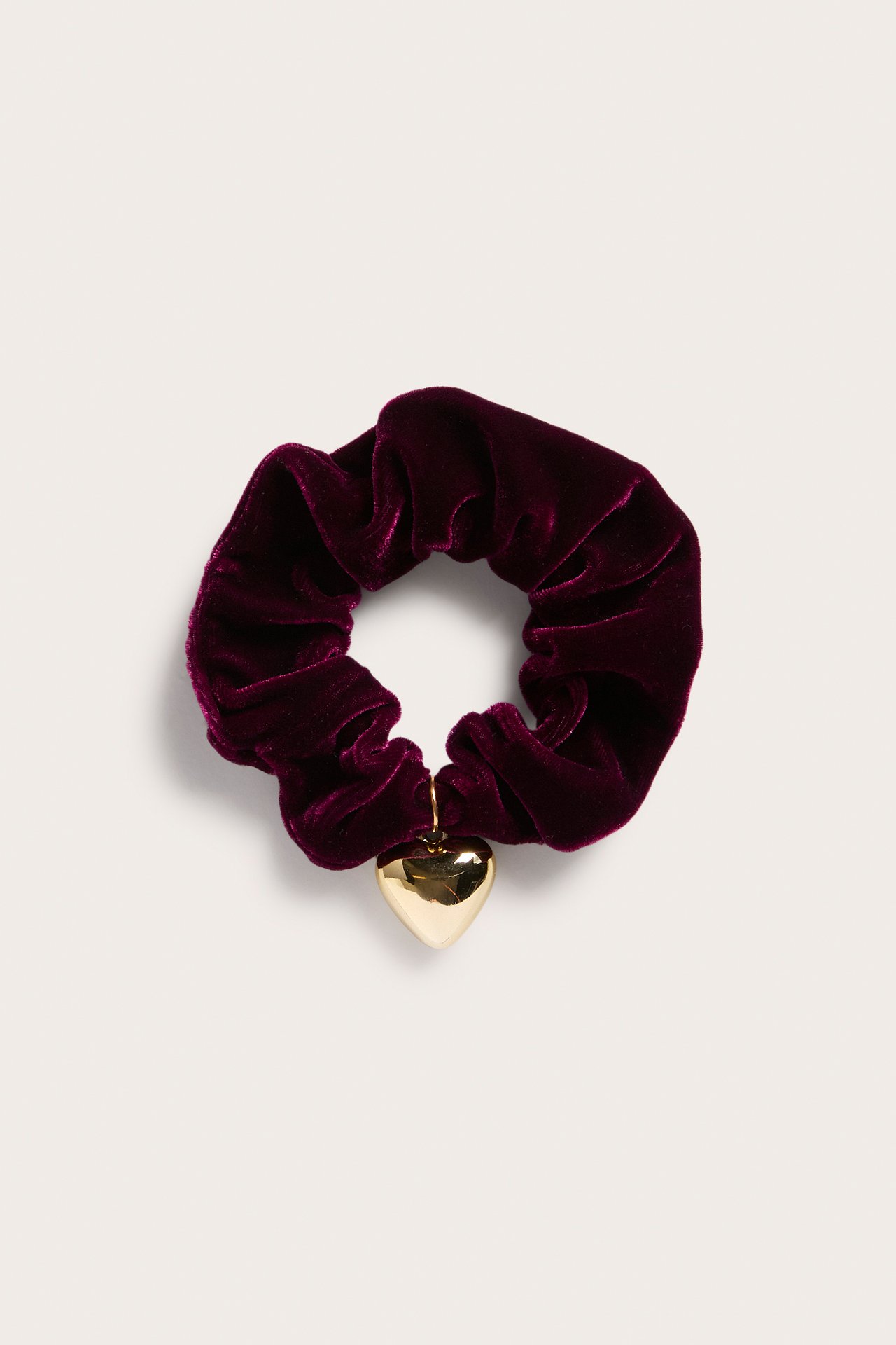 Uppifrånvy av en mörkröd sammetsscrunchie med ett glänsande guldhjärta.