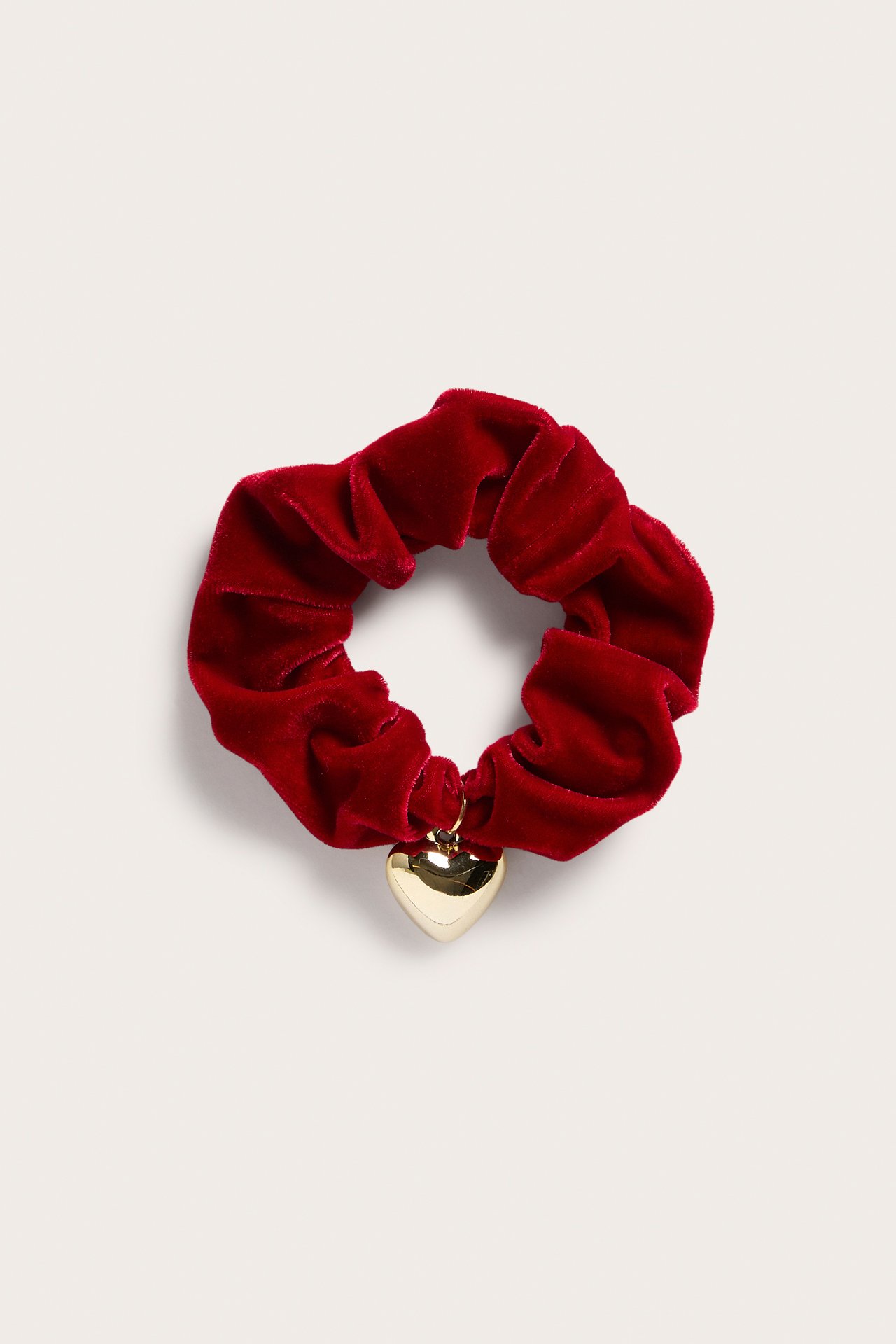 Närbild av en röd sammets-scrunchie med ett guldhjärta.
