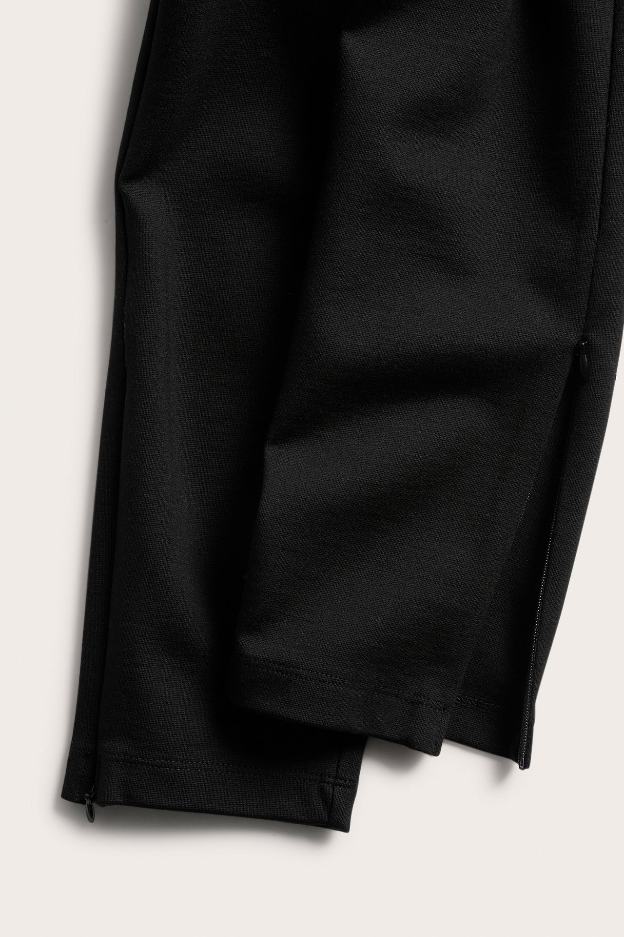 Nærbilde av ensfargede svarte leggings med skjulte glidelåser ved anklene.