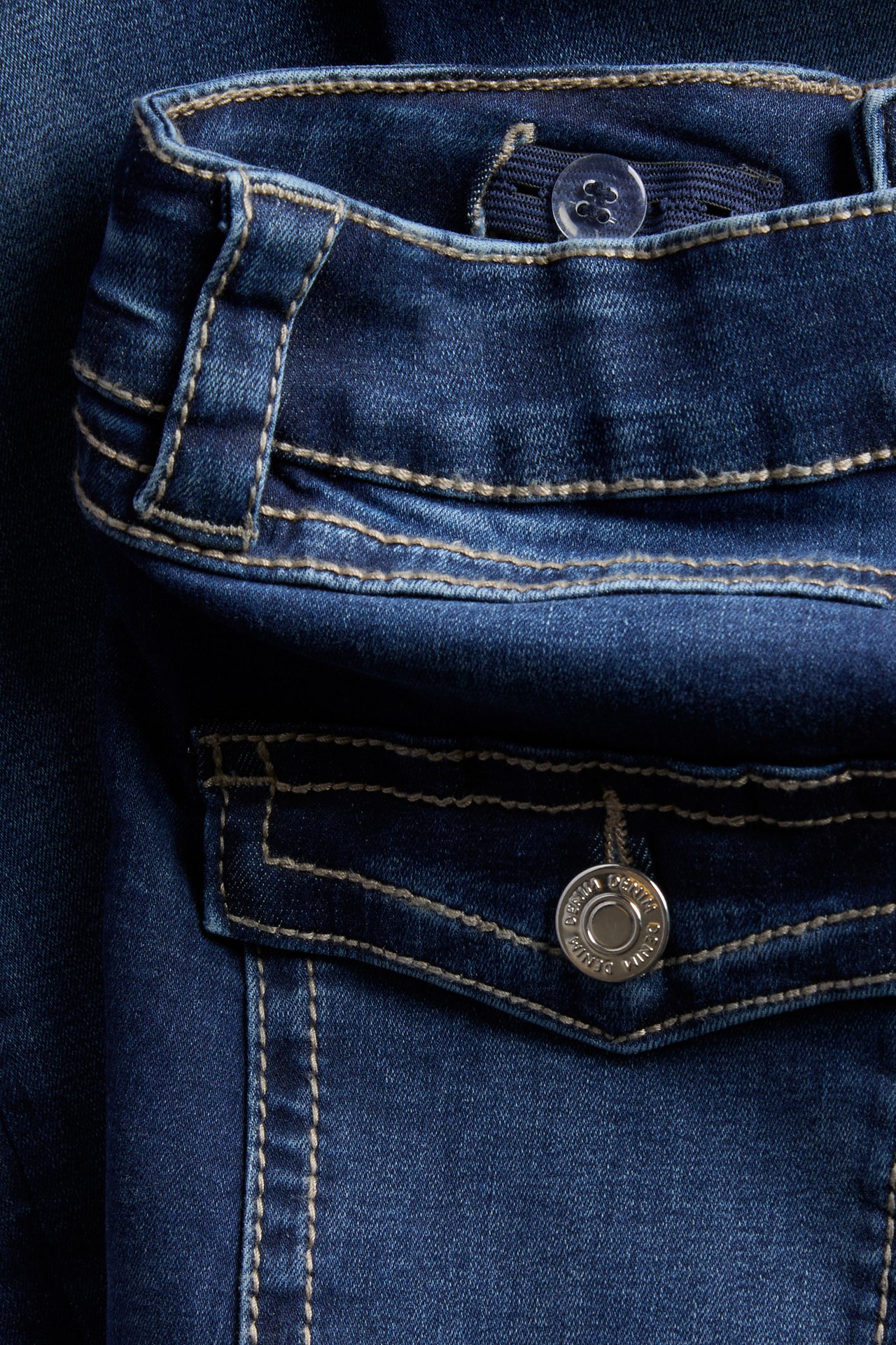 Lähikuva tummansinisistä denimfarkuista, joissa säädettävä nappivyötärö ja metallinapillinen tasku.