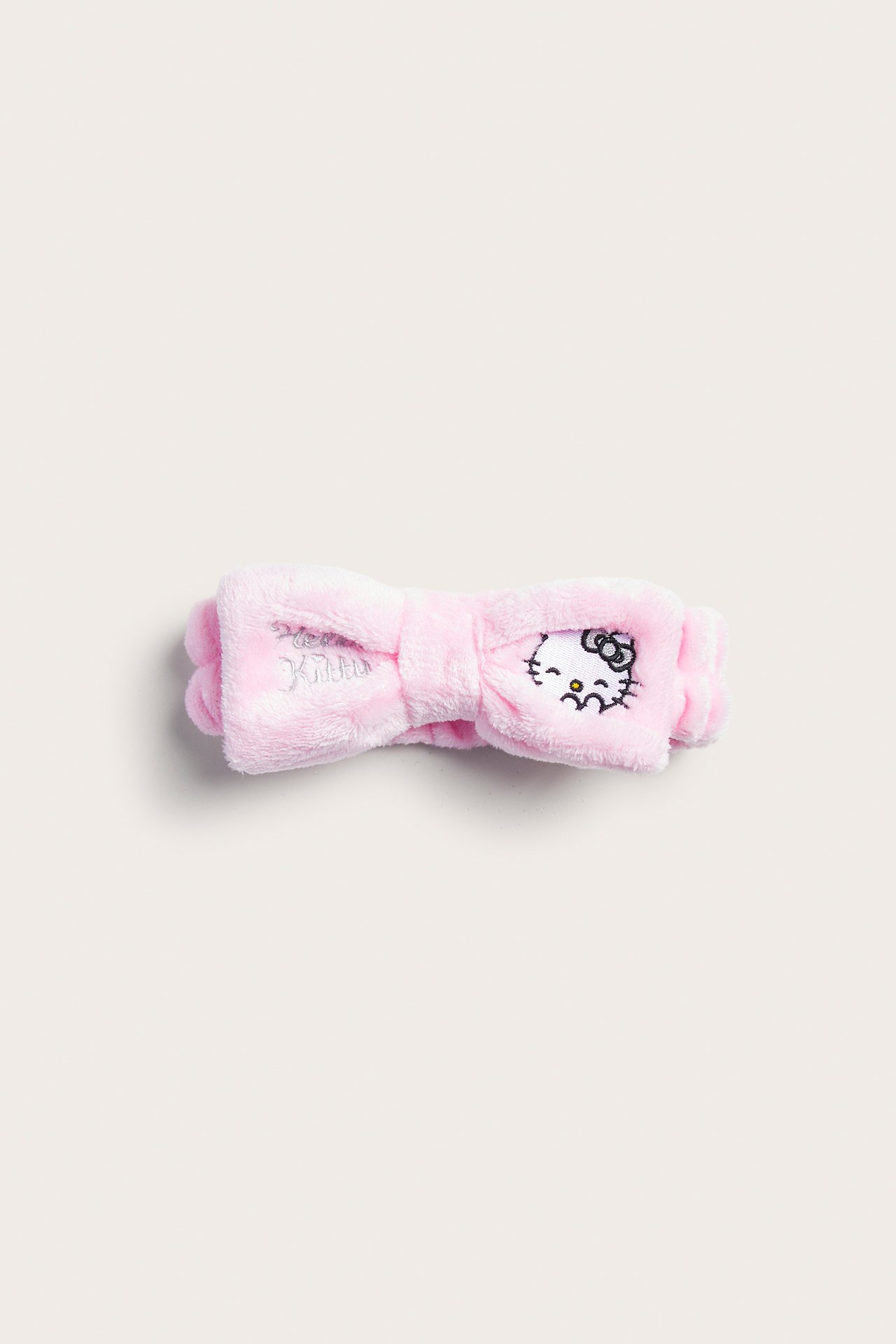Widok z przodu różowej, puszystej opaski na włosy Hello Kitty z kokardą i haftem.