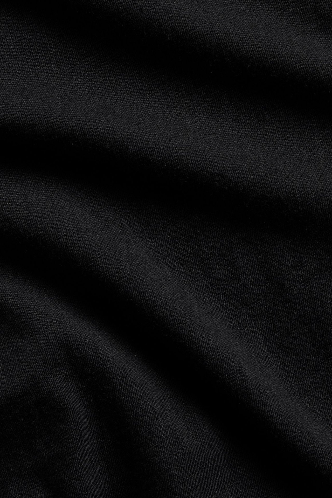 Lähikuva mustasta, yksivärisestä puuvillaisesta t-paitakankaasta kevyillä laskoksilla.