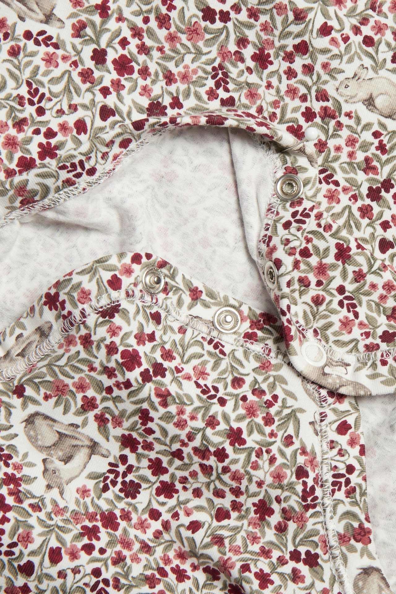 Närbild på en vit babybody med rött blommigt mönster, kaniner och tryckknappar.