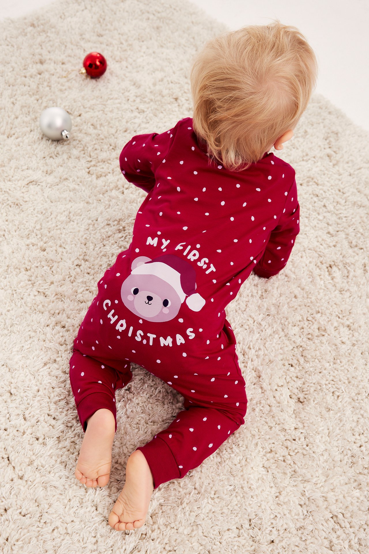 Baby i röd prickig pyjamas med "My First Christmas"-björnprint, bakifrån.