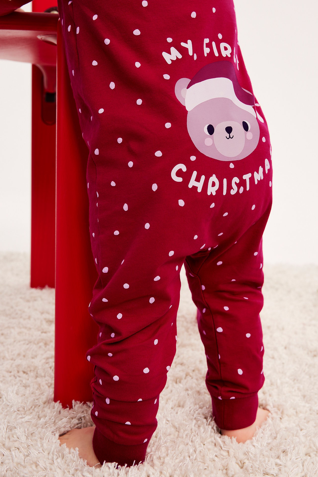 Närbild bakifrån på en rödprickig babyoverall med 'My, Fir Christmas'-björntryck.