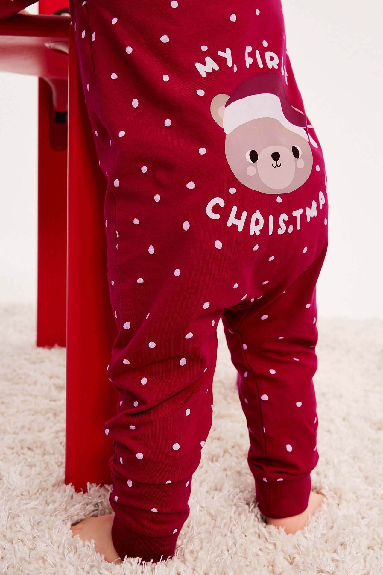 Nærbilde bakfra av en baby i rød prikkete pyjamas med julebjørnmotiv.