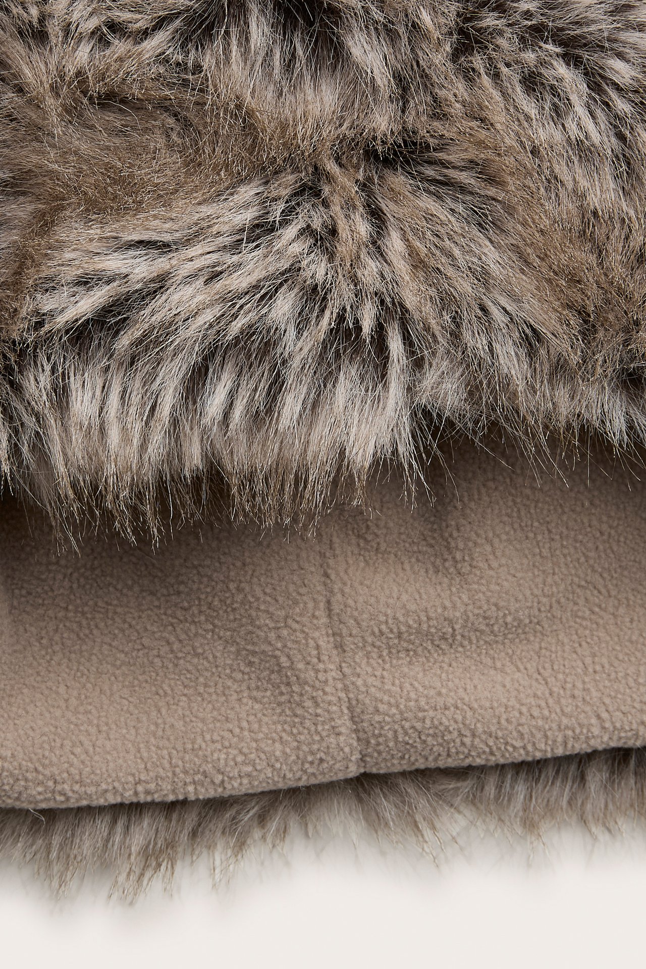 Nærbilde av rufsete brun og beige fuskepels med lys brunt fleecemateriale under.
