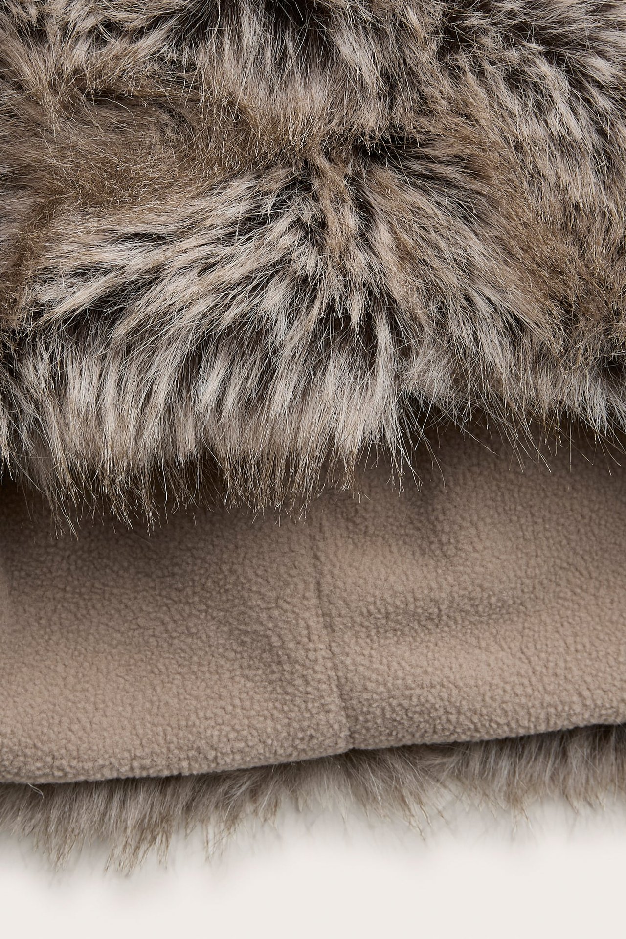 Nærbilde av rufsete brun og beige fuskepels med lys brunt fleecemateriale under.