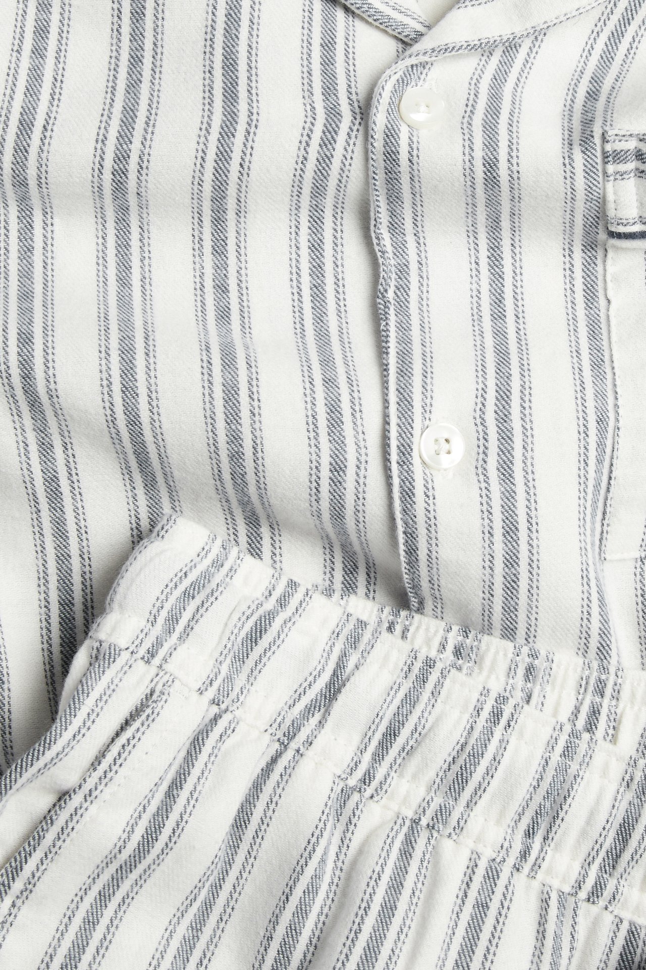 Nærbilde av hvit- og blåstripete pyjamasskjorte med knapper og matchende elastiske shorts.