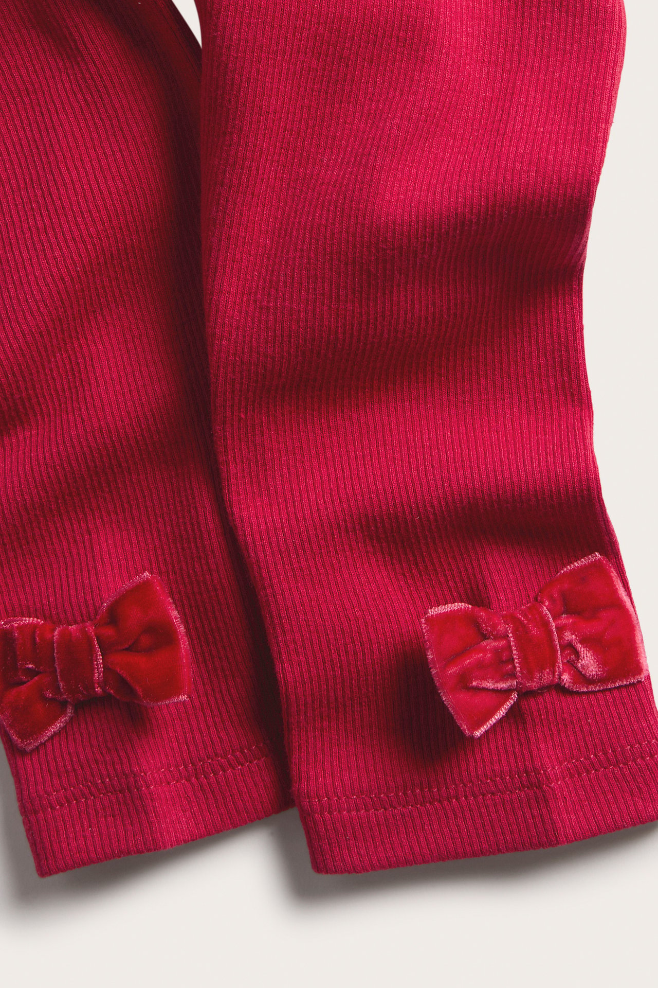 Närbild på röda ribbade leggings för barn med sammetsrosetter vid anklarna.