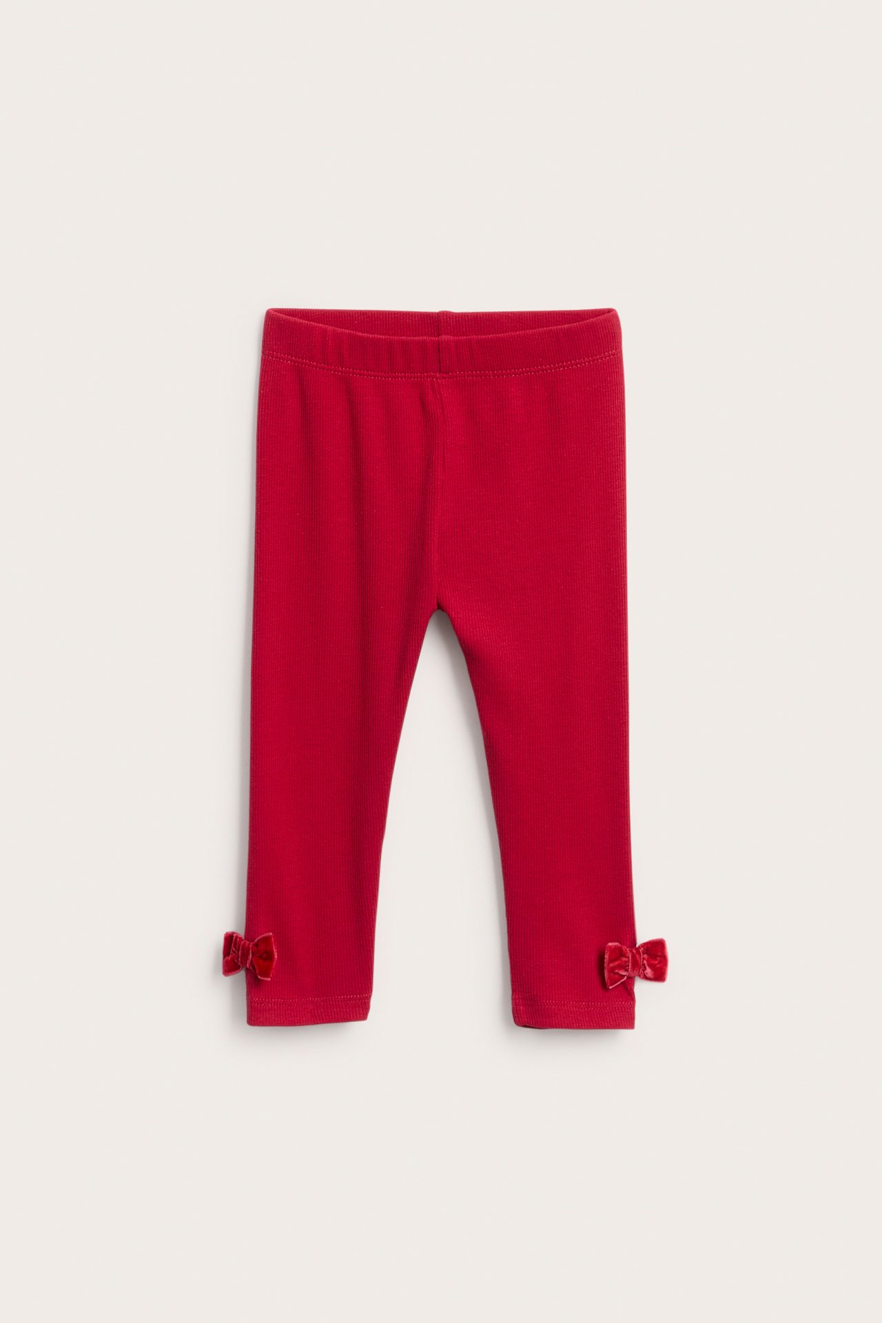Framsida av röda ribbade baby leggings med små sammetsrosetter vid anklarna.
