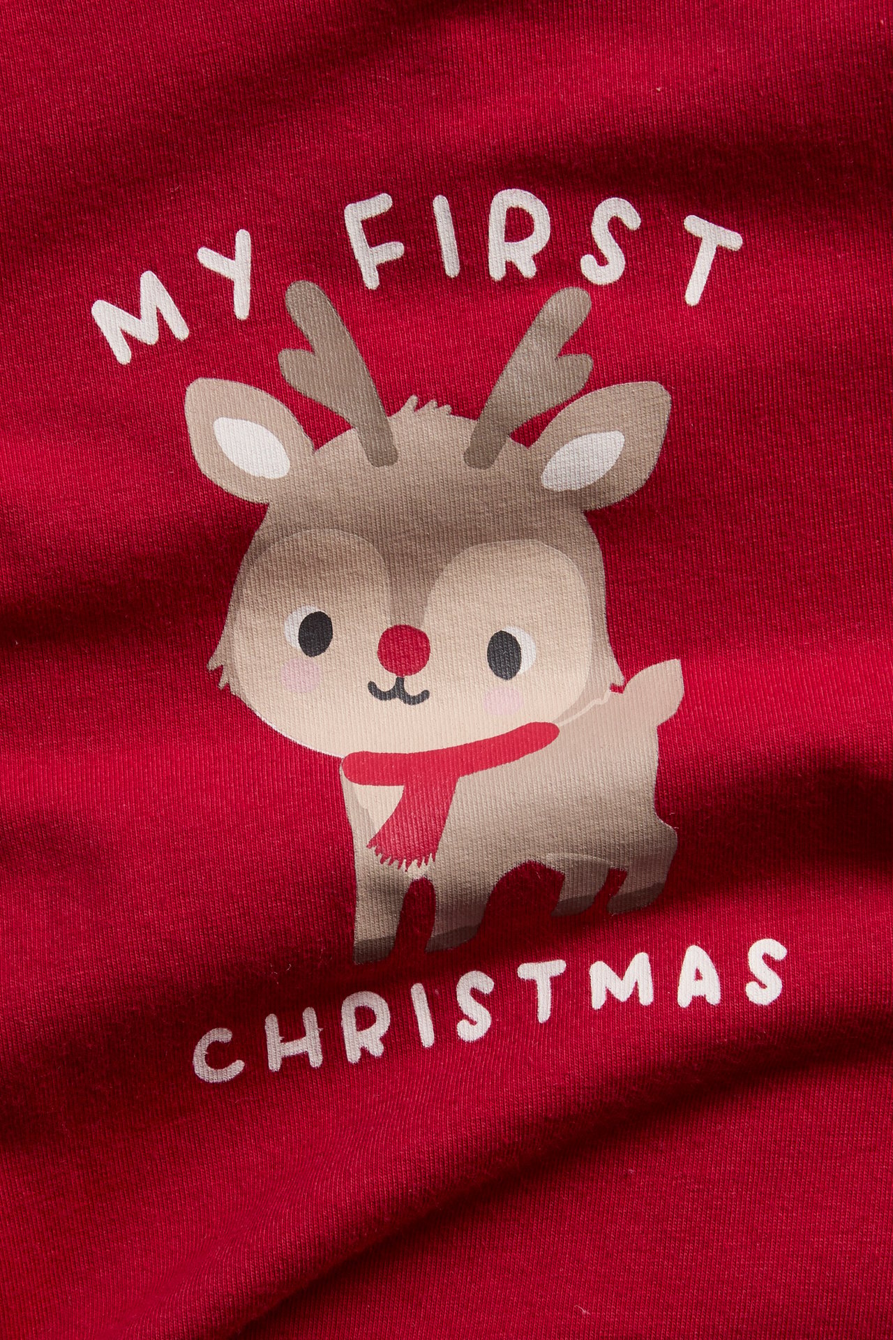 Zbliżenie czerwonego ubranka niemowlęcego z nadrukiem renifera 'MY FIRST CHRISTMAS'.