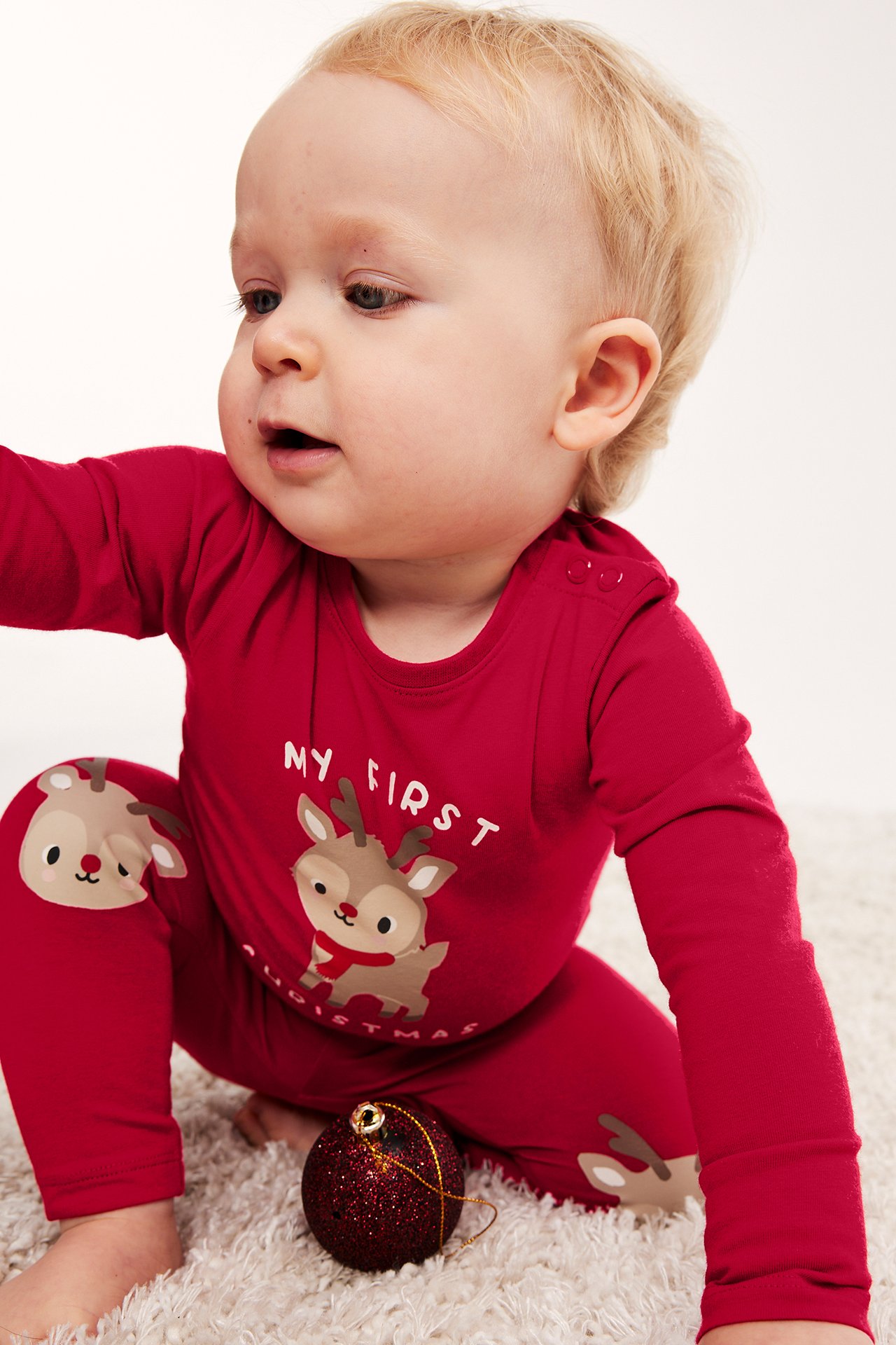 Widok z przodu dziecka w czerwonym body 'My First Christmas' i pasujących legginsach z reniferami.