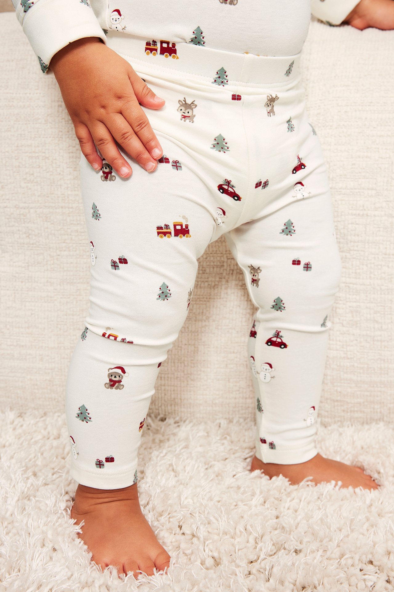 Närbild framifrån på en baby i vit julmönstrad pyjamas.