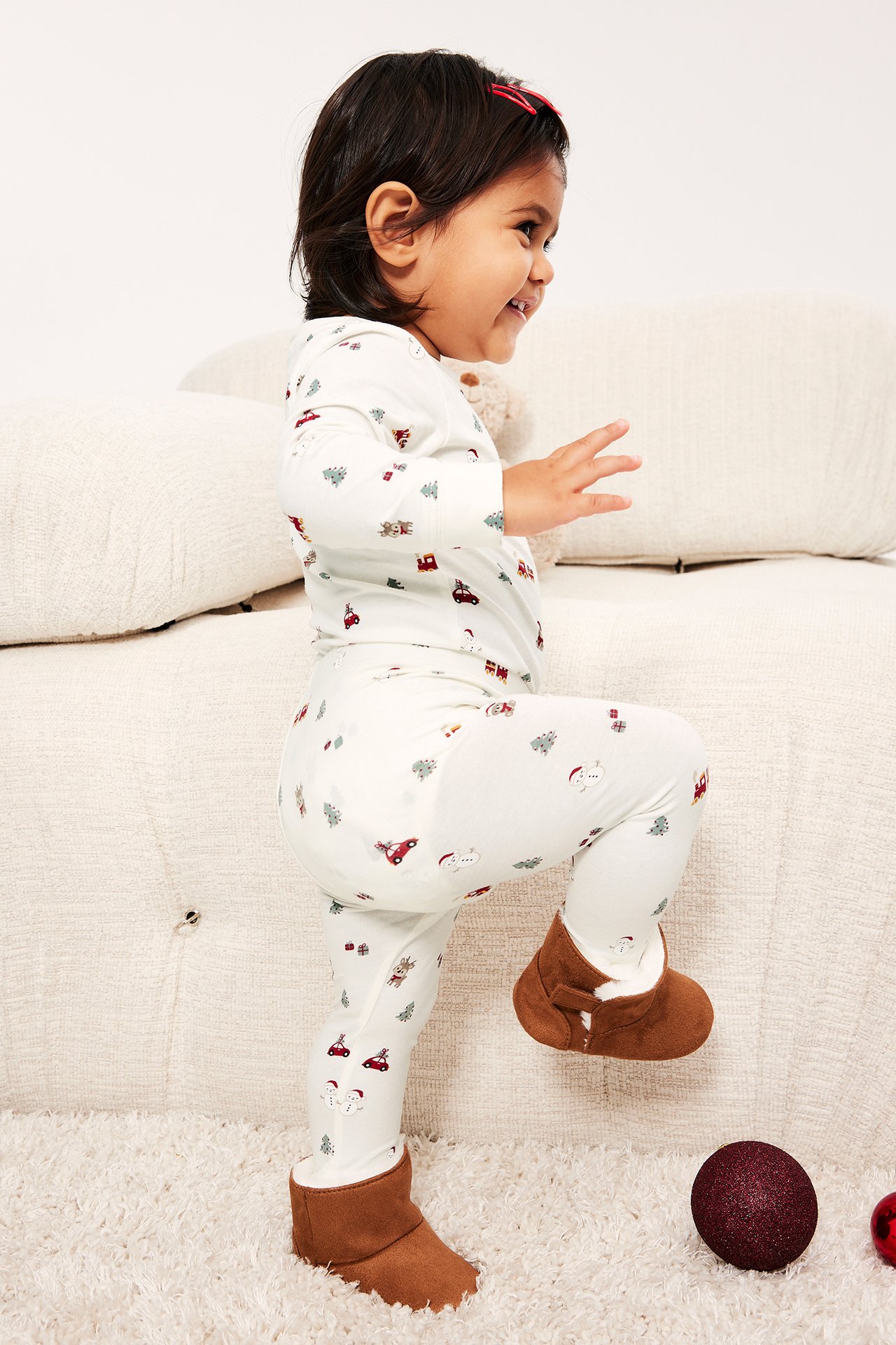 Sidovy av ett baby i en vit julmönstrad pyjamas och bruna tossor.