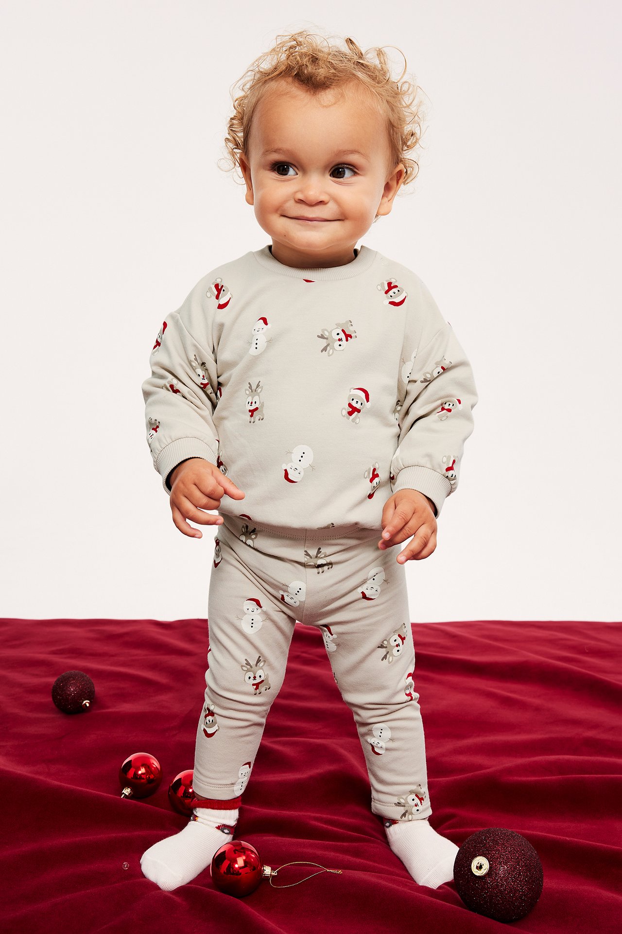 Framifrån, baby i ljusbeige långärmad tröja och matchande leggings med jultryck.