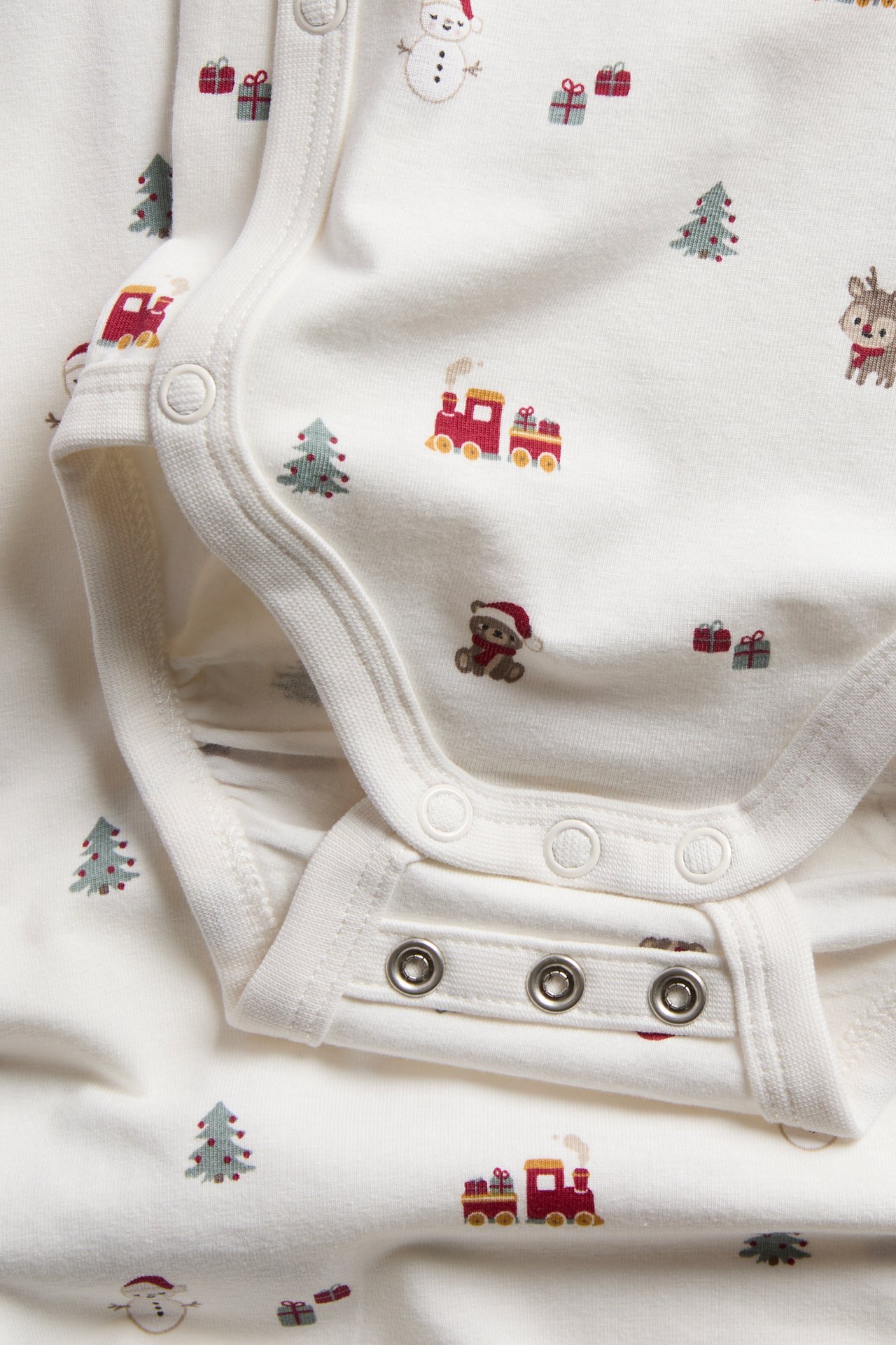 Närbild av en cremefärgad babybody i bomull med jultryck och tryckknappar.