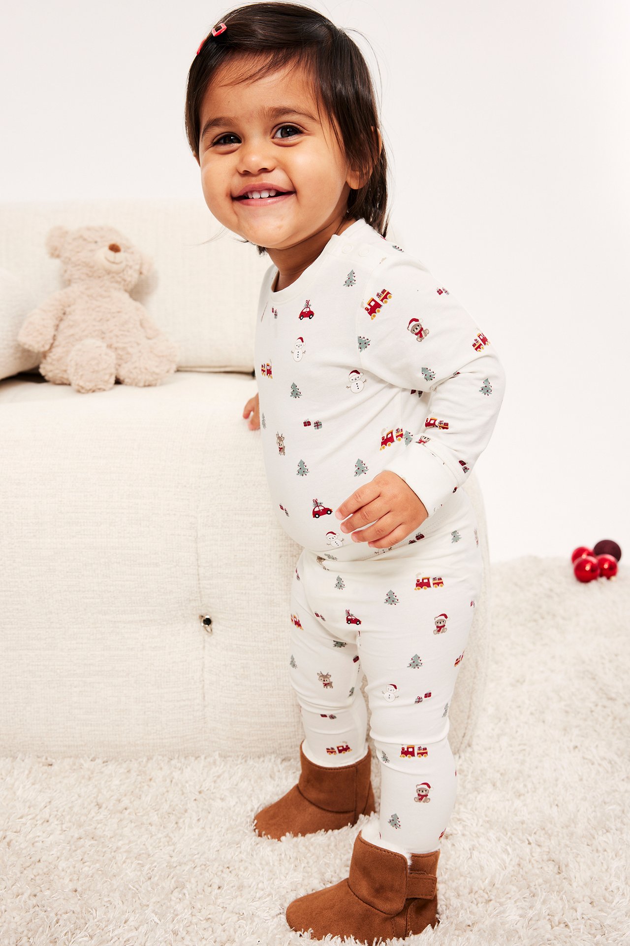 Framifrån, baby i vita pyjamasar med jultryck och bruna stövlar.