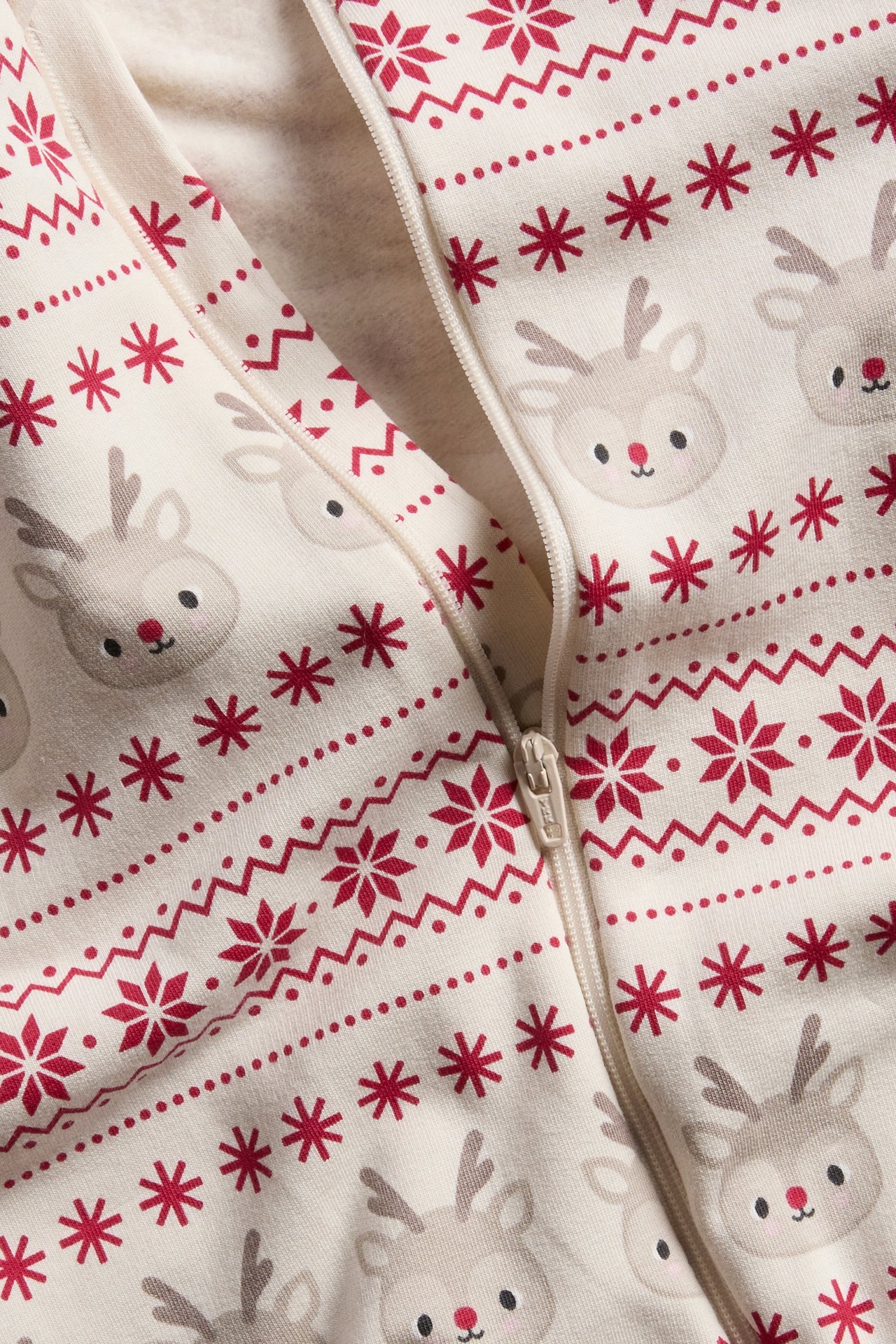 Närbild av en gräddvit babypyjamas med rött ren- och snöflingsmönster, med dragkedja.