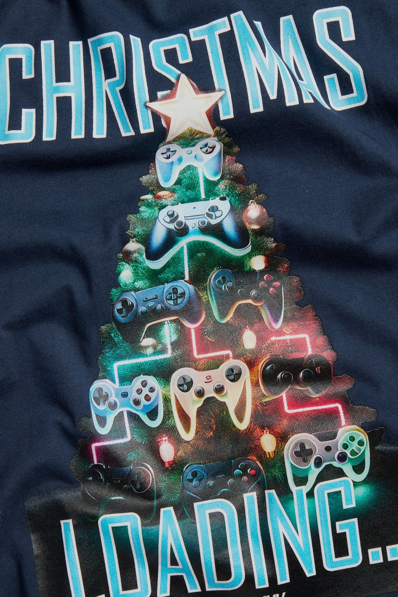 Närbild på mörkblå t-shirt med speltkontroll-julgransprint och texten 'CHRISTMAS LOADING...'.