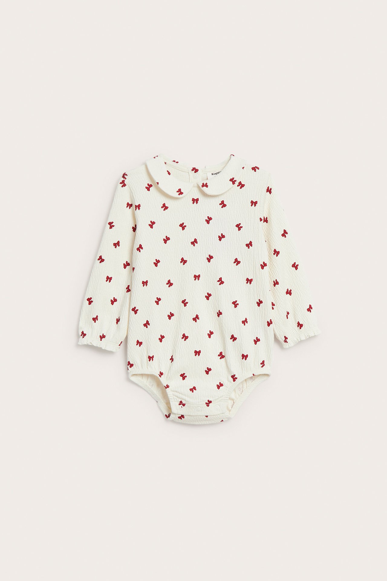 Framifrån, en krämfärgad babybody med lång ärm, rött rosettmönster och rundad krage.