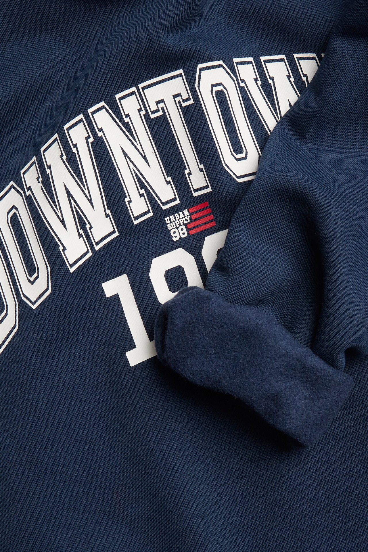 Närbild på en marinblå sweatshirt med fleecefoder och vitt 'DOWNTOWN URBAN SUPPLY 98'-tryck.