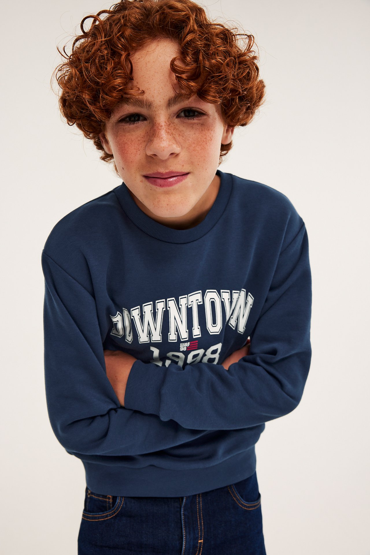 Framsida av barn som bär en mörkblå sweatshirt med 'DOWNTOWN 1998'-tryck och mörkblå jeans.