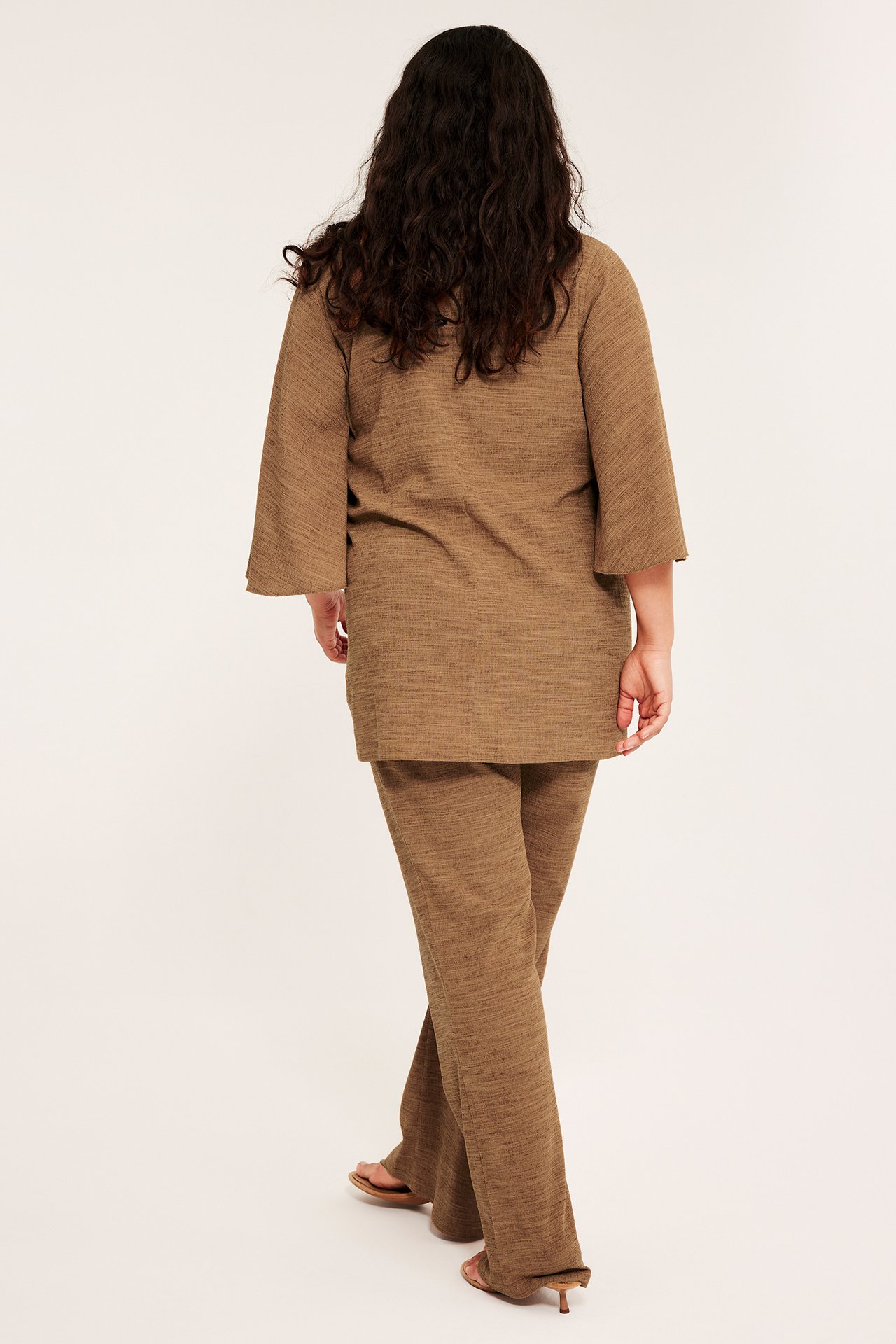 Nainen takaa ruskeissa bootcut-jerseypull-on-housuissa, yhteensopivassa tunikatopissa ja korkokengissä.