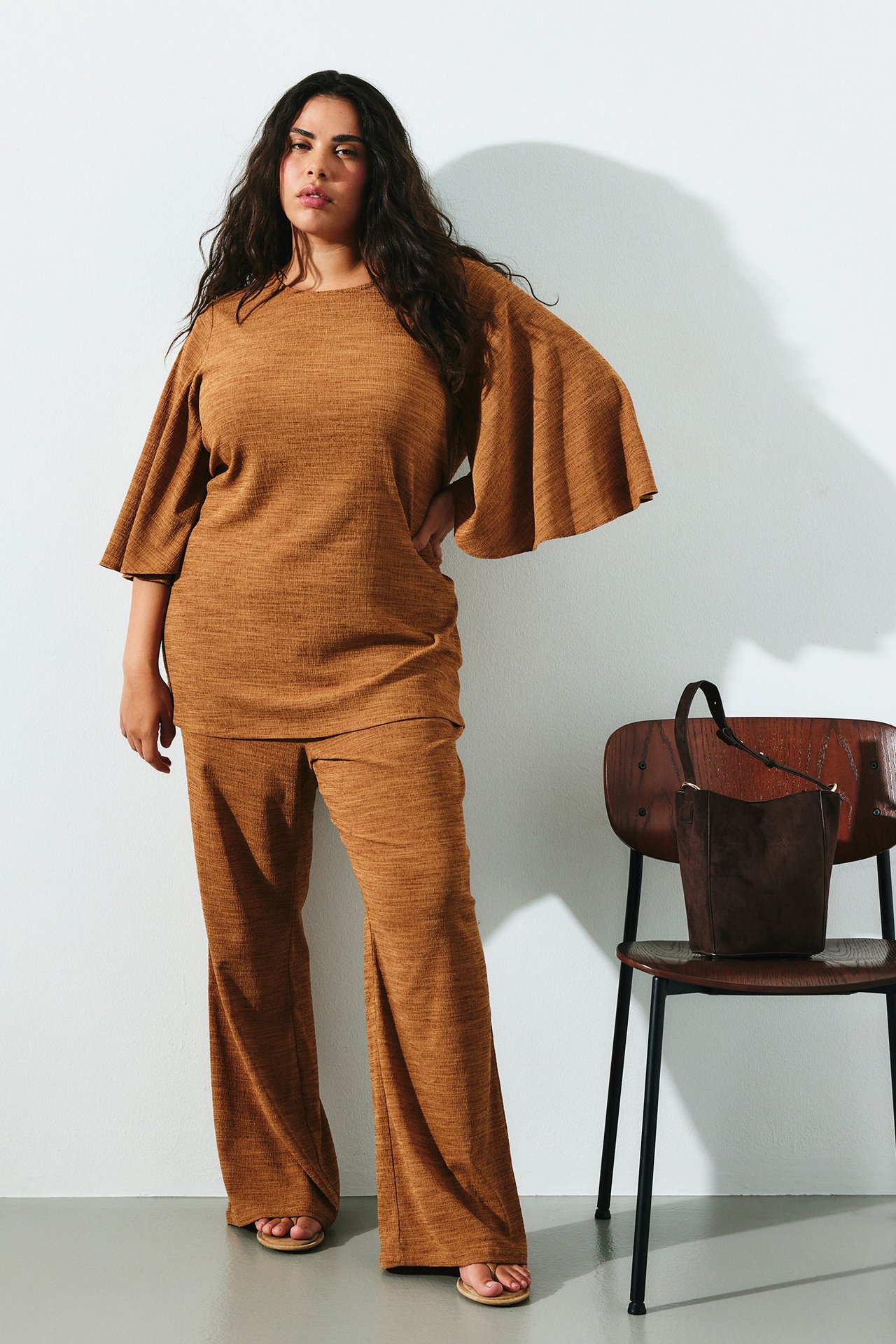 Naisen etukuva ruskeissa bootcut-jerseyhousuissa ja yhteensopivassa yläosassa, jossa on levenevät hihat.
