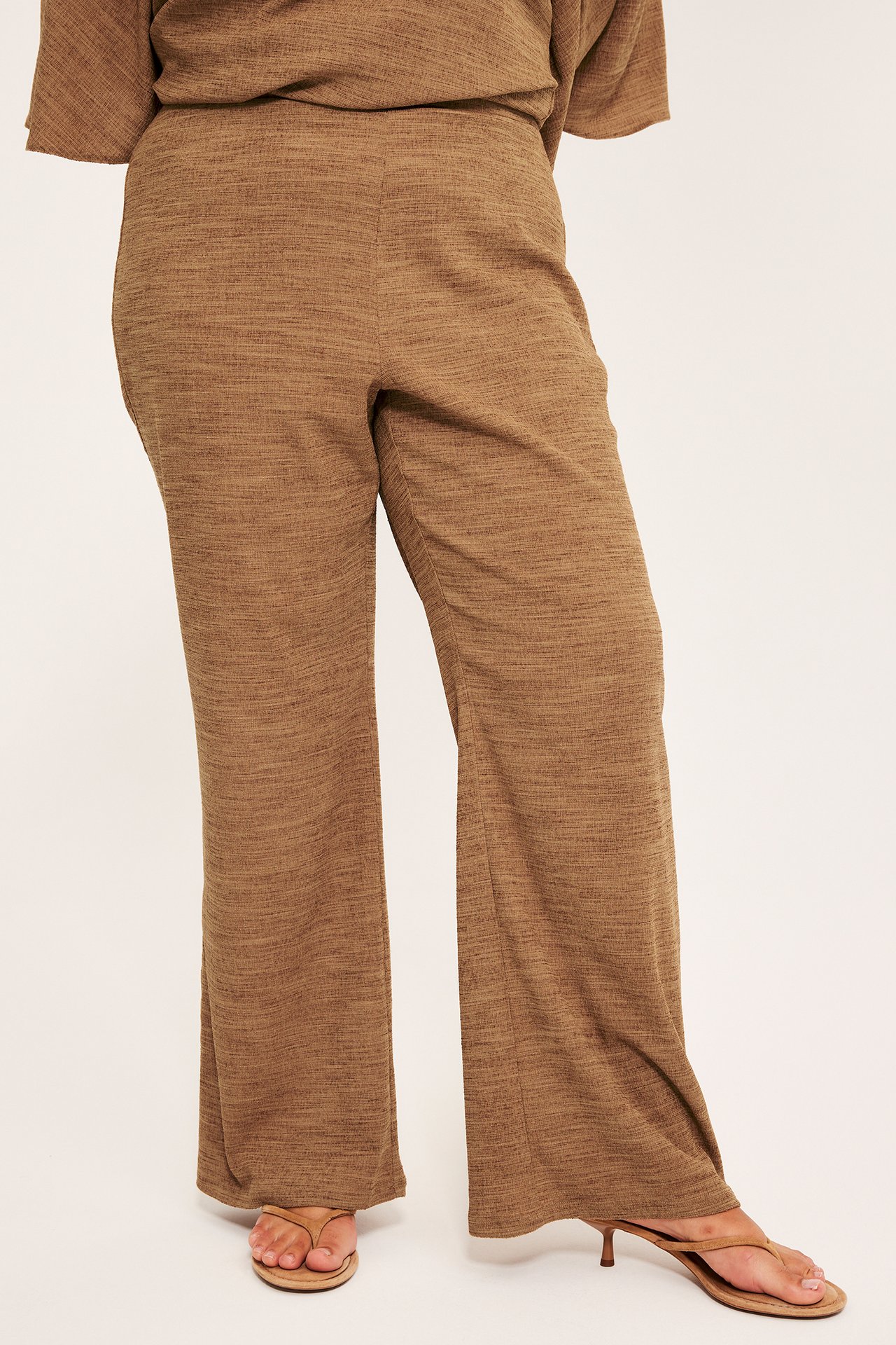 Naisen etukuva ruskeissa tekstuurisissa jersey bootcut-housuissa, yhteensopivassa paidassa, korollisissa sandaaleissa.