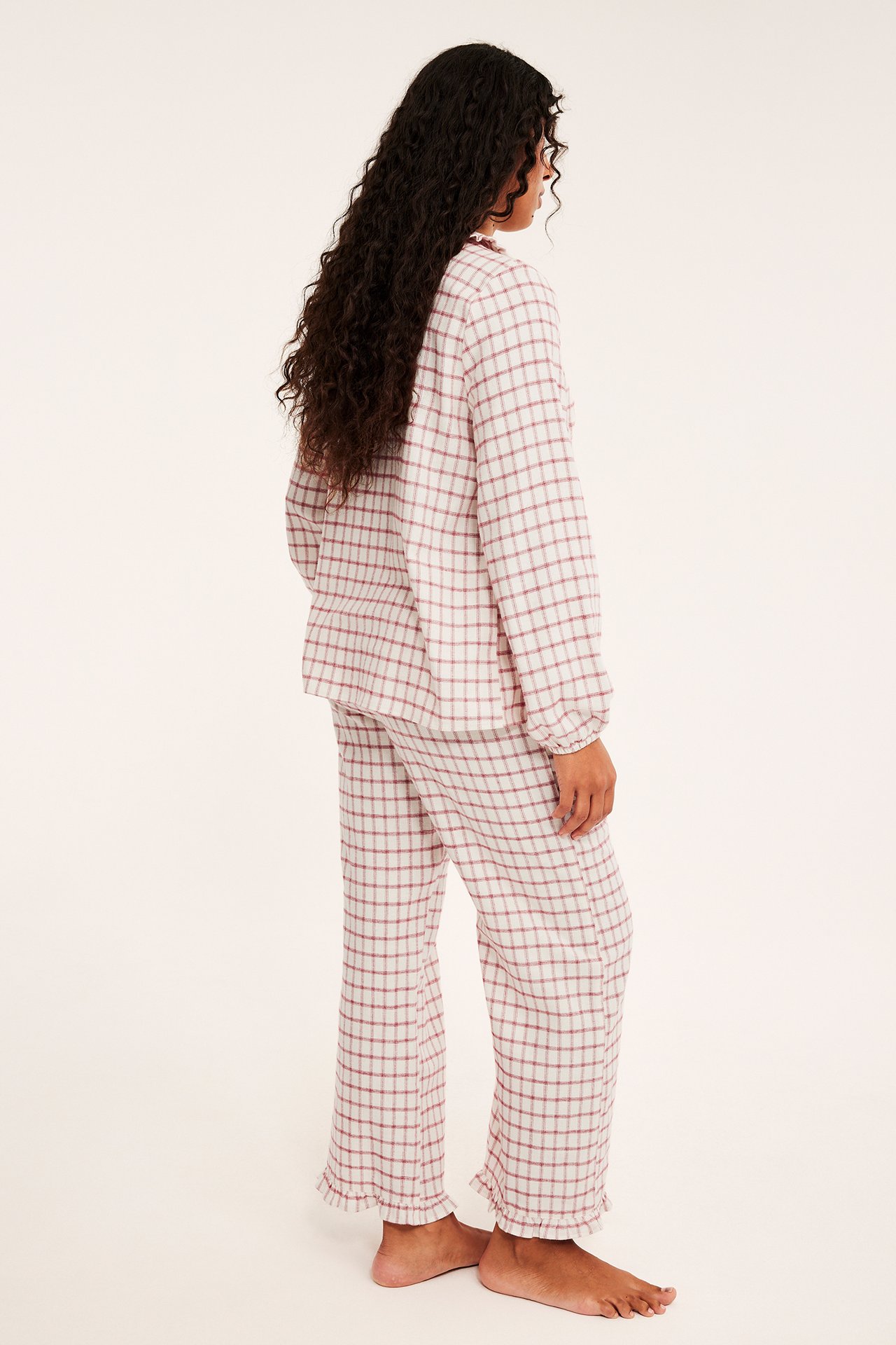 Sivukuva naismallista yllään valko-punainen ruudullinen pyjama röyhelöreunoilla.