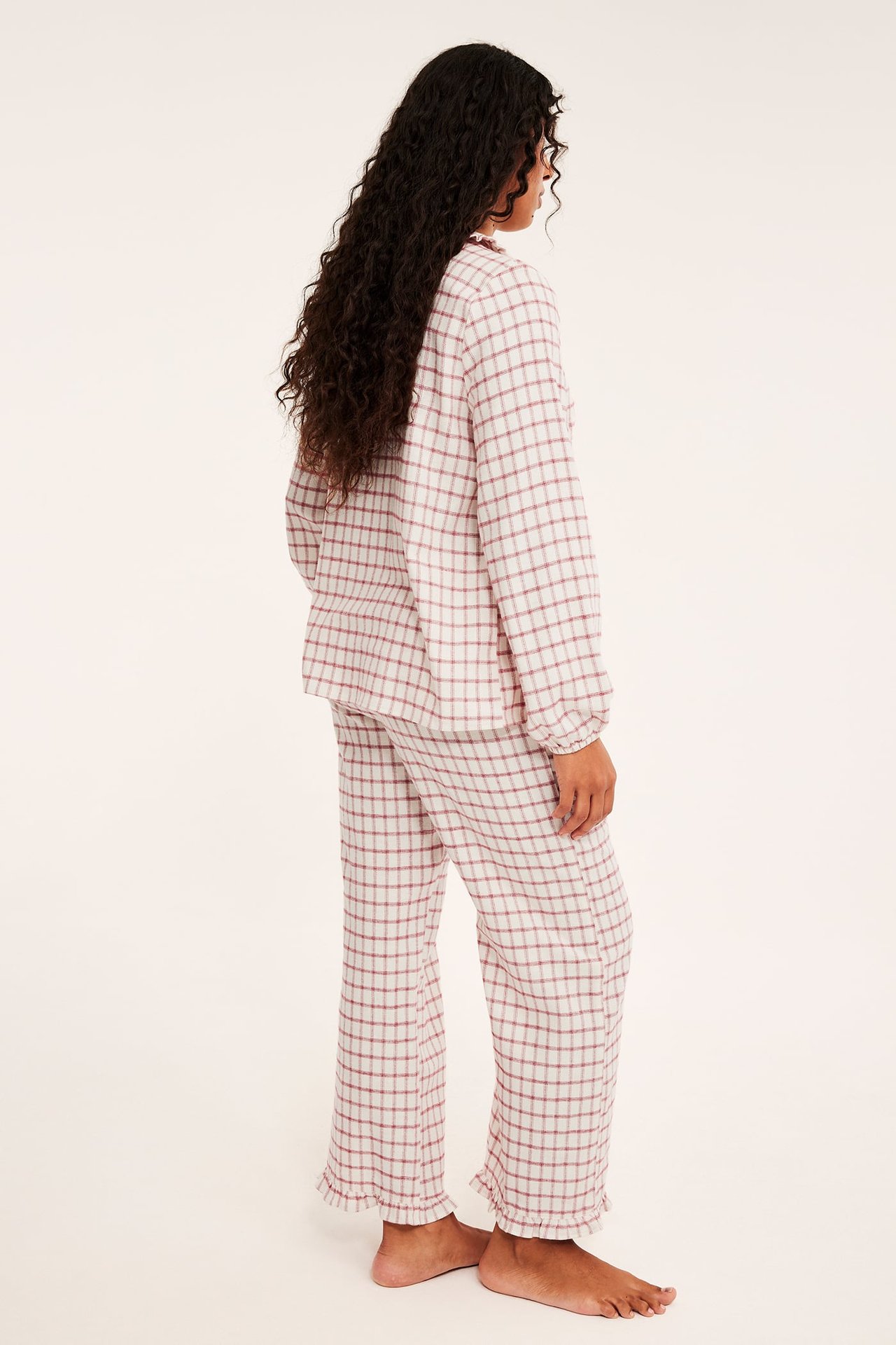 Sivukuva naismallista yllään valko-punainen ruudullinen pyjama röyhelöreunoilla.
