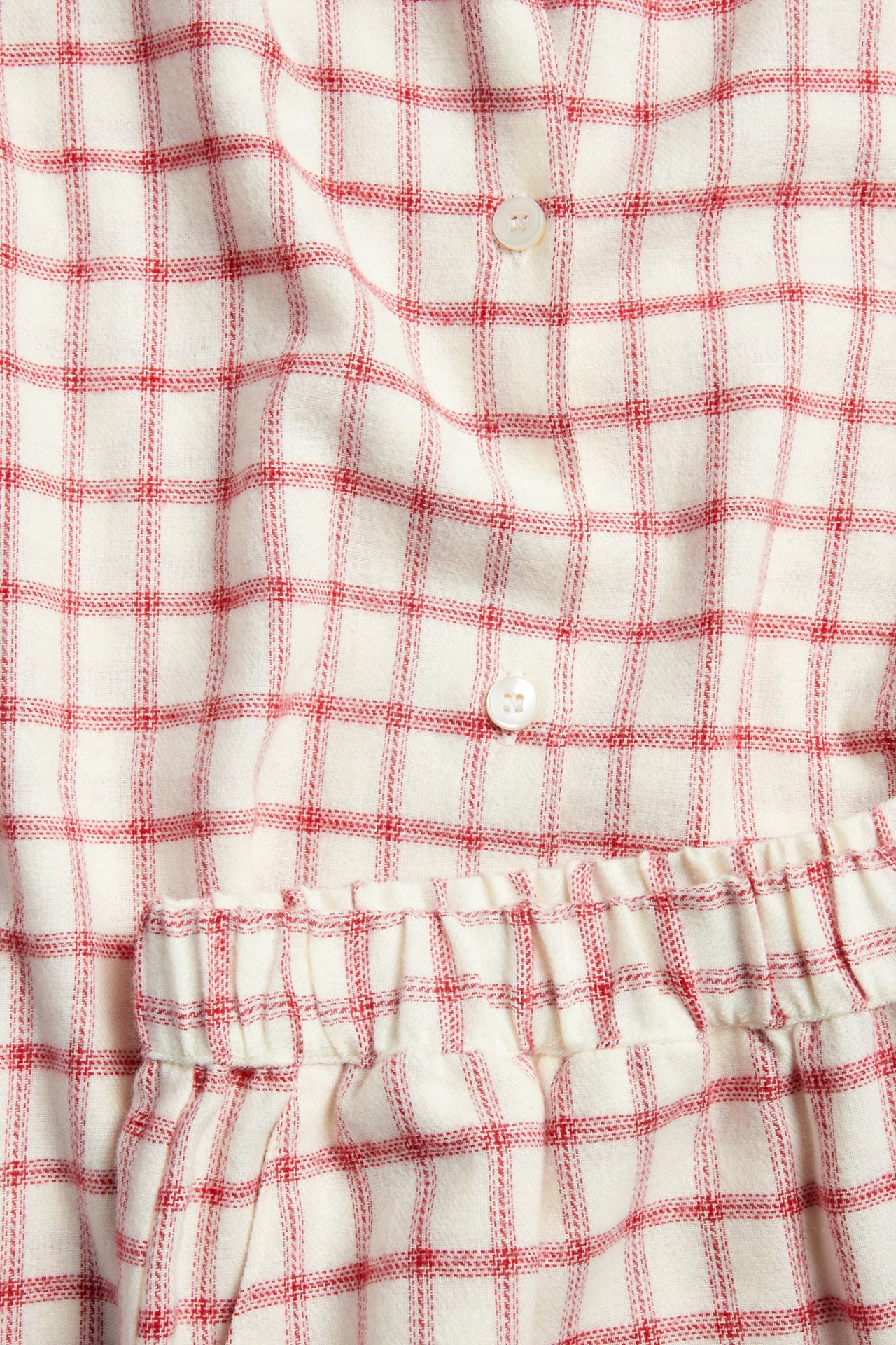 Lähikuva punavalkoruudullisesta pyjamasetistä, jossa on valkoiset napit ja joustava vyötärö.