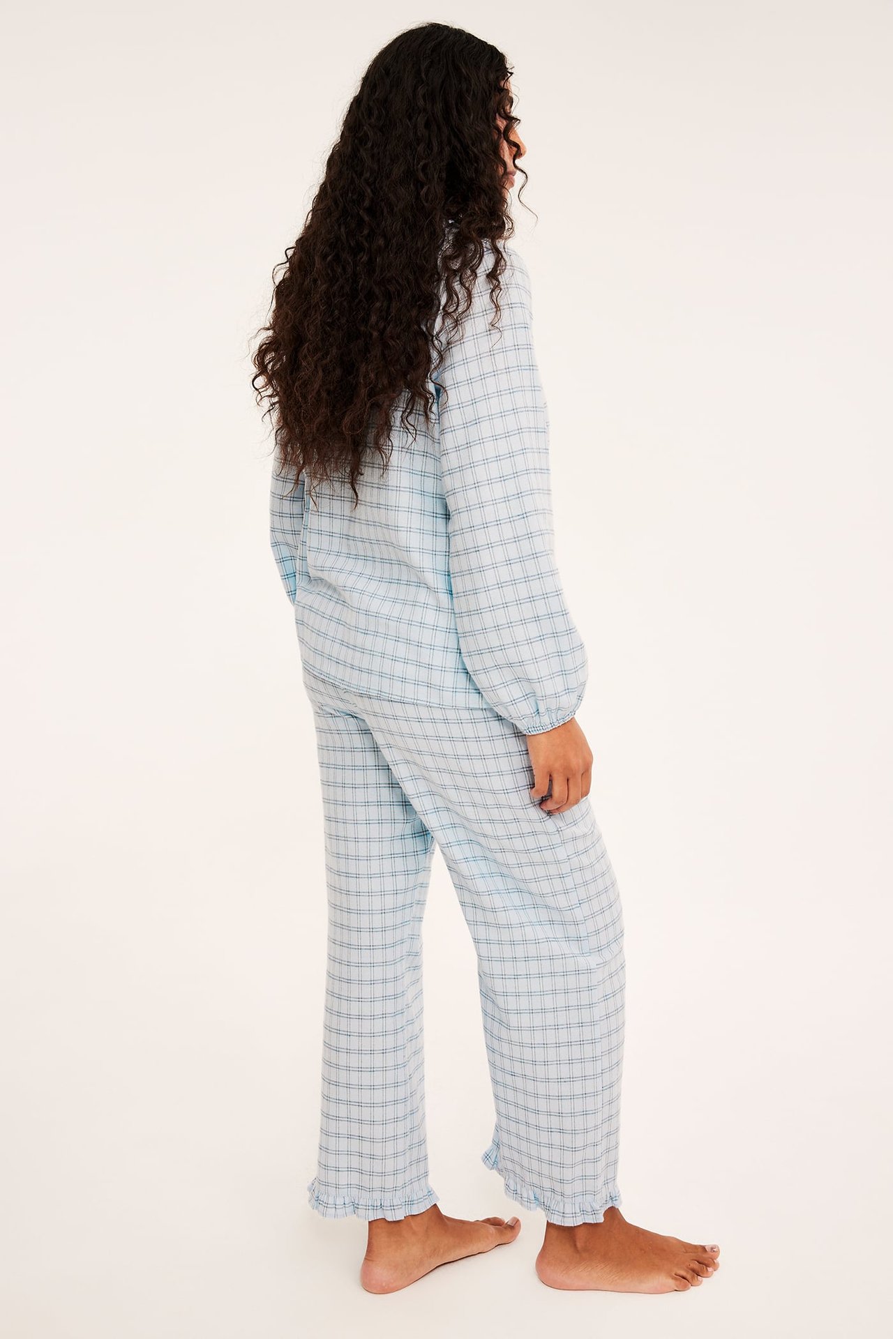 Sivukuva naisesta yllään vaaleansininen ruudullinen pitkähihainen pyjamassetti.