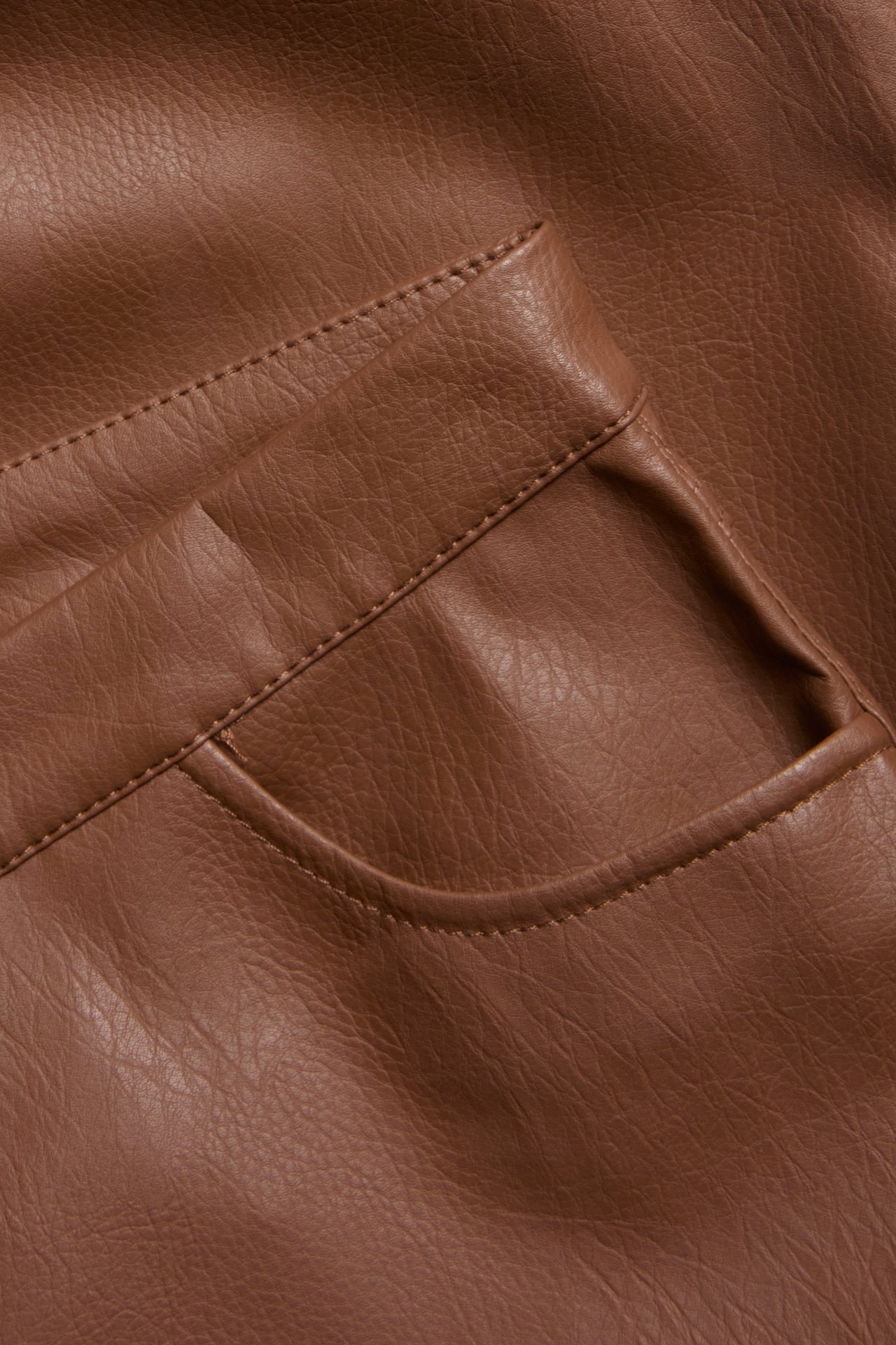 Närbild av ett brunt texturerat konstlädermaterial med sömmar och en rundad ficka.