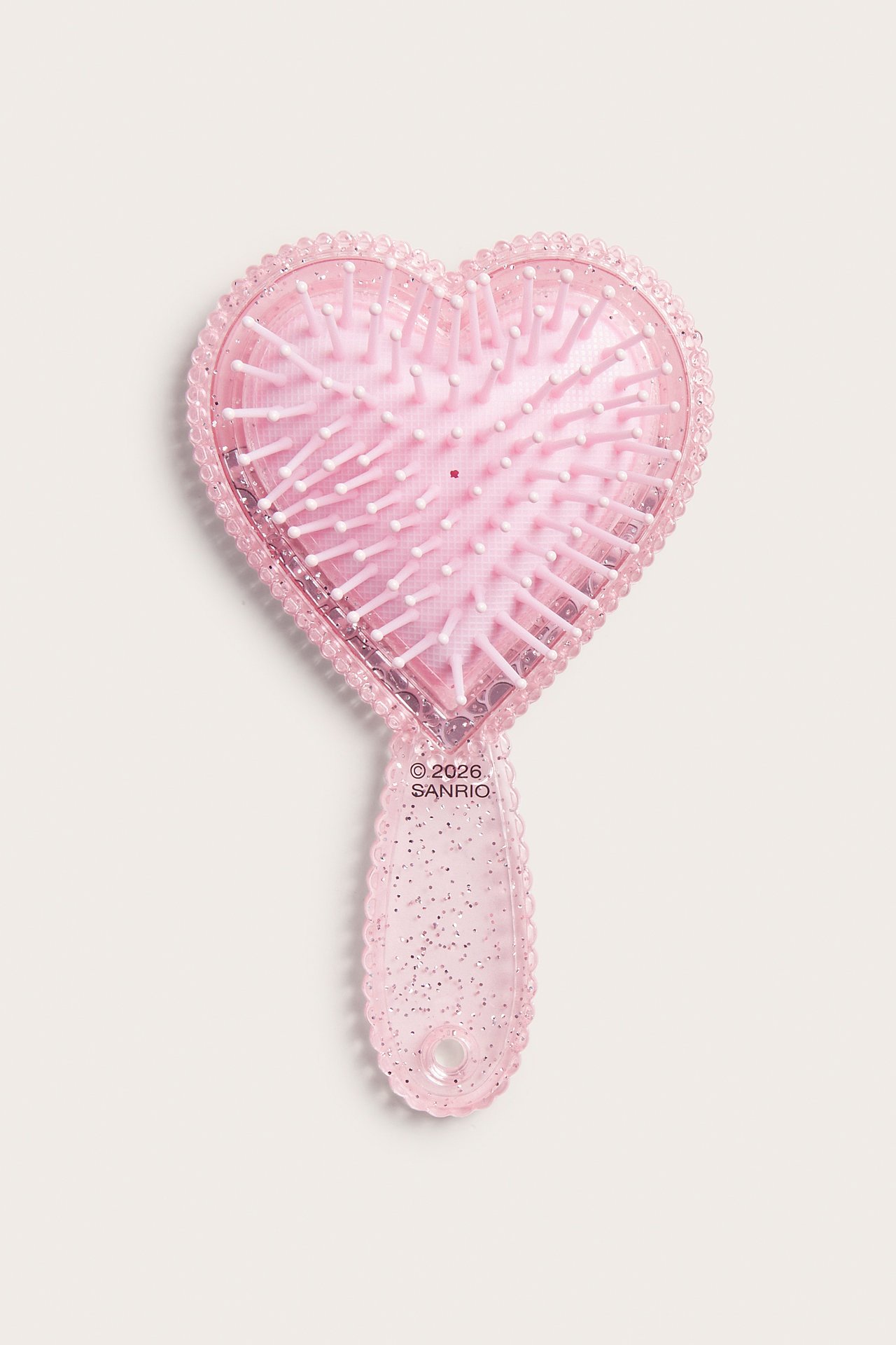Rosa glittrig hjärtformad hårborste med Sanrio-text, uppifrån sett.